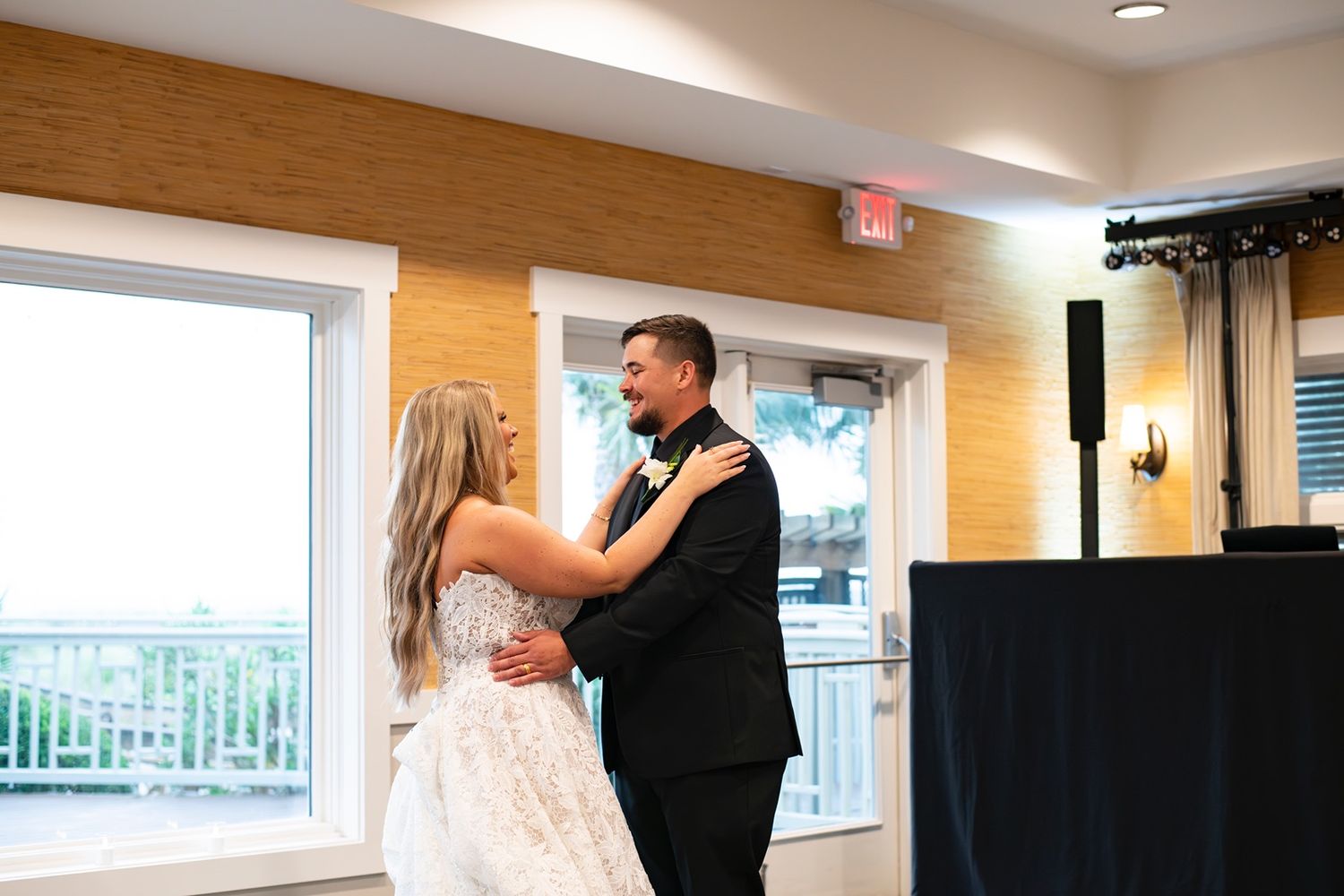 A couple shares their first dance in an elegant reception venue with natural light streaming through windows.