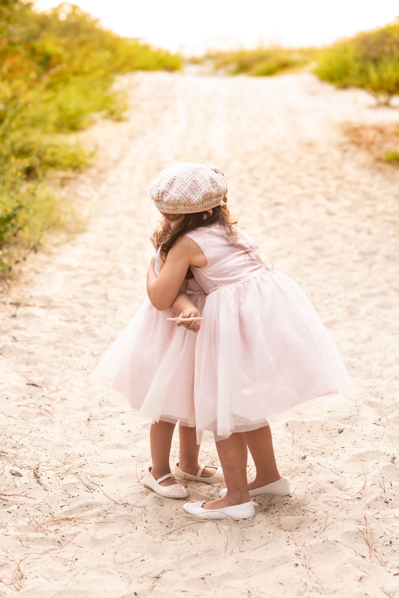 Small child in pink tulle dress sitting on sandy beach path in romantic vintage style photo series.