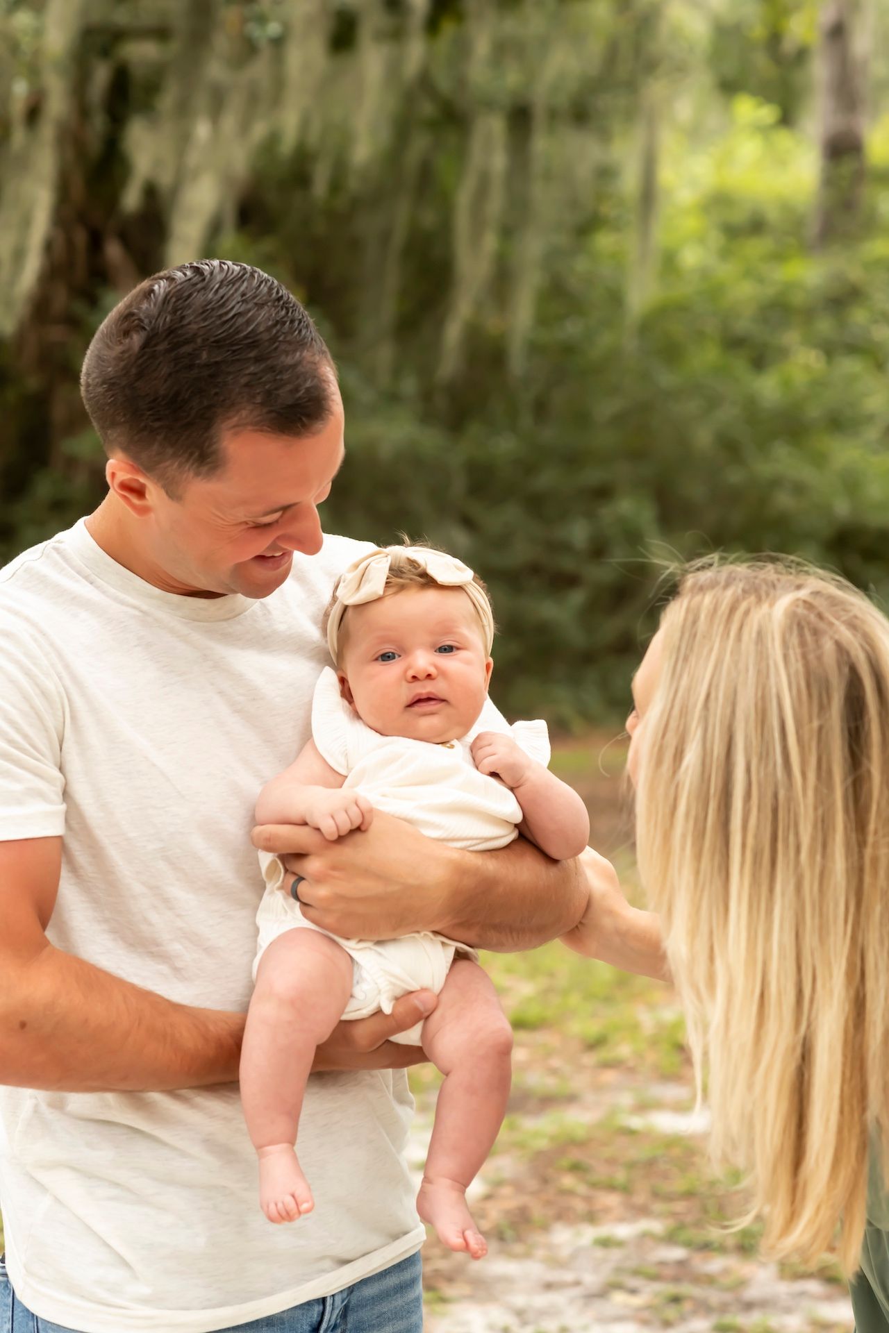 A family moment captured outdoors in a natural wooded setting with soft sunlight filtering through the trees.
