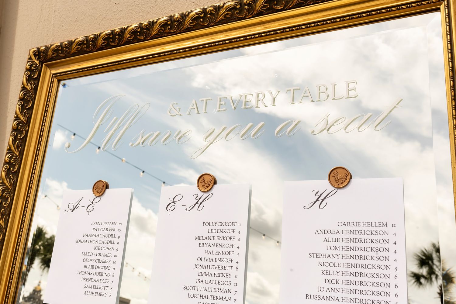 Elegant gold-framed seating chart display with table assignments for wedding guests.