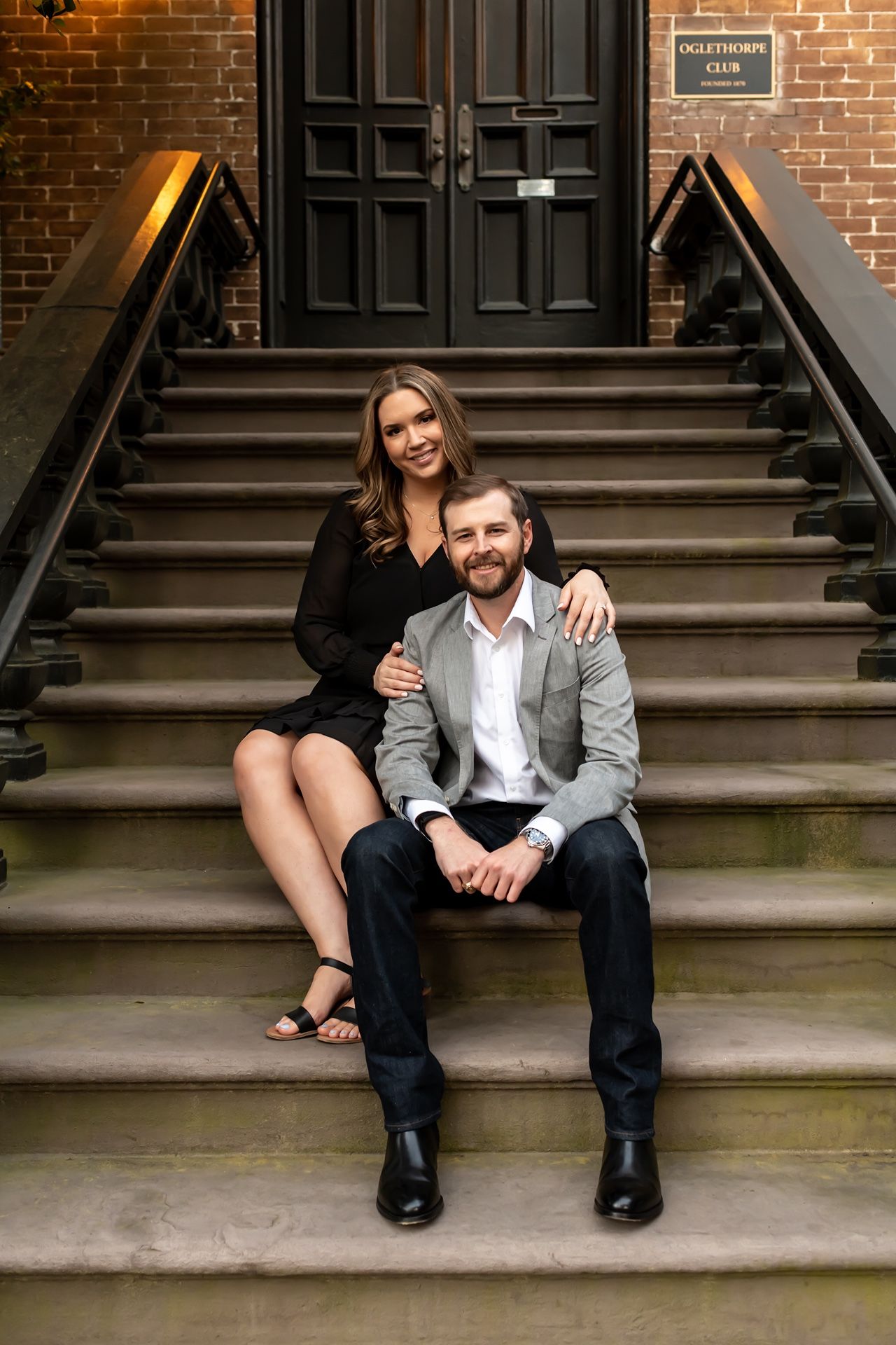 Couple sits playfully on brick building steps during an urban engagement photo session.