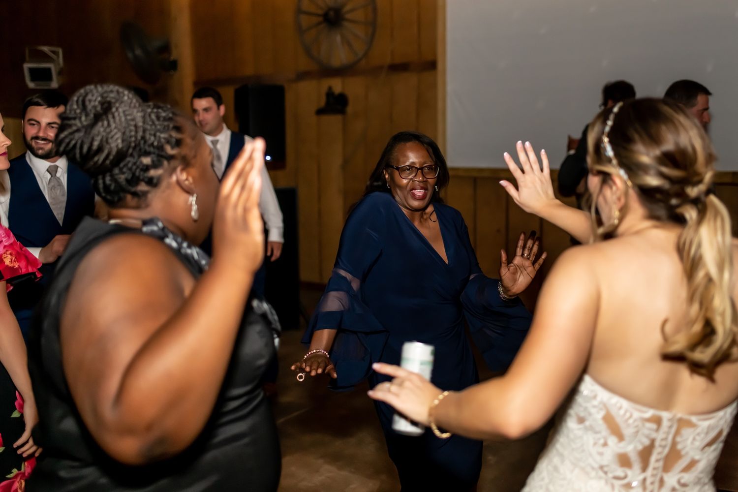 Wedding reception guests celebrate joyfully on a dance floor inside a rustic-style venue with warm lighting.