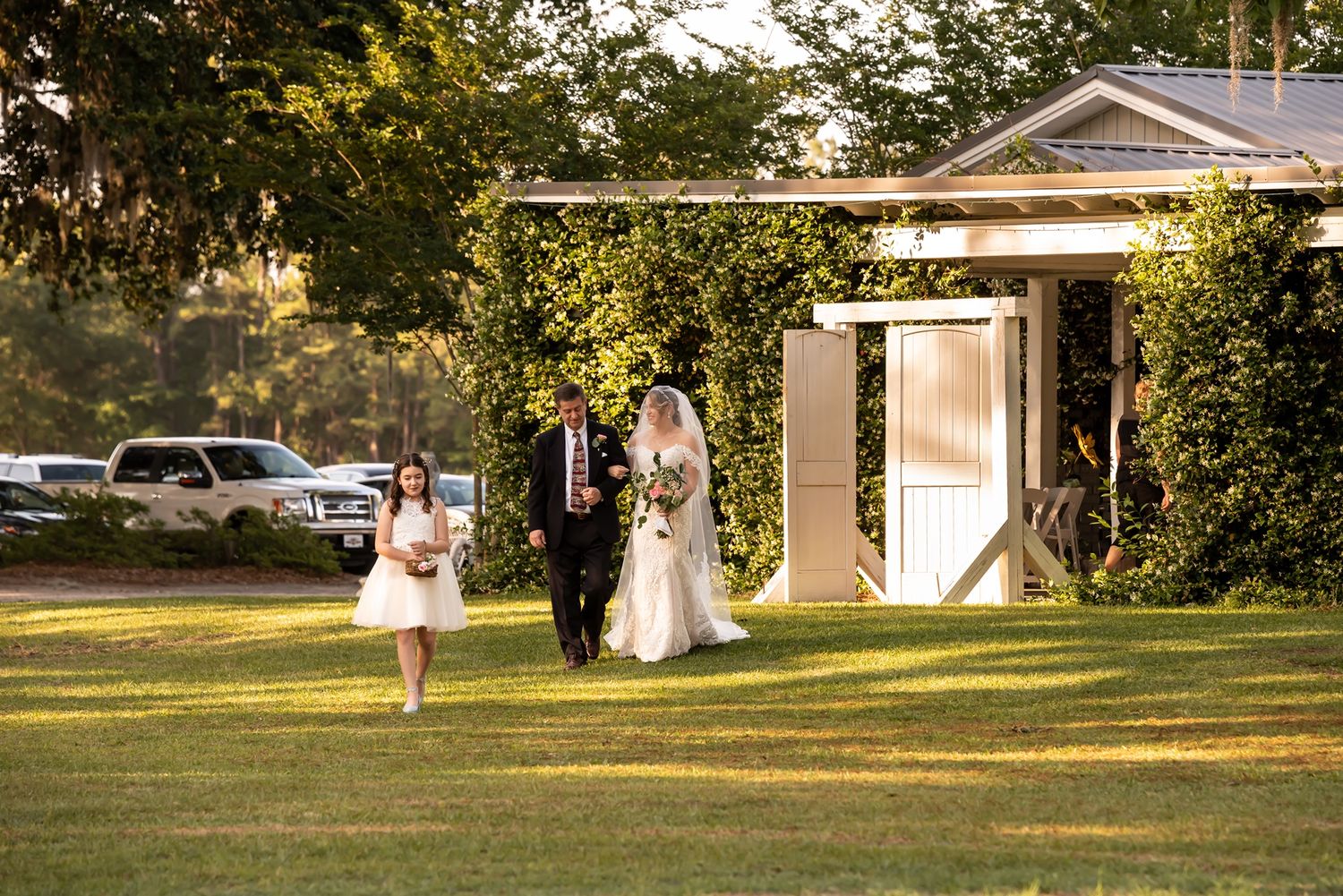 A scenic outdoor summer celebration takes place on a lush green lawn next to a white building at golden hour.