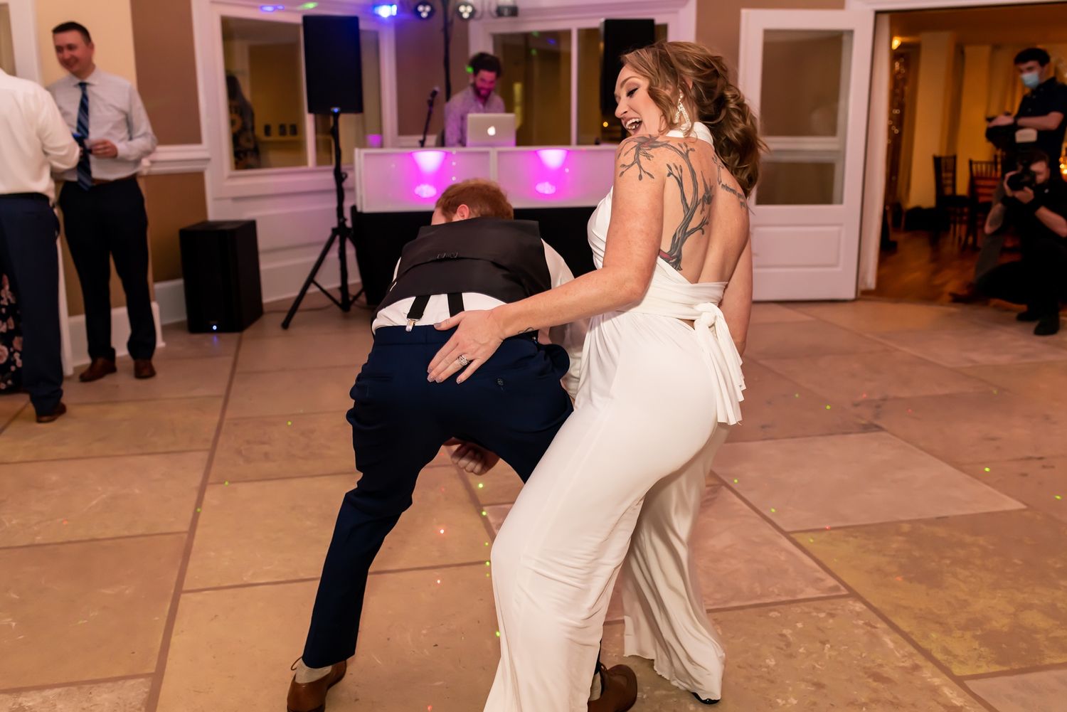 A couple performs a playful dance move during their wedding reception on a tiled floor.