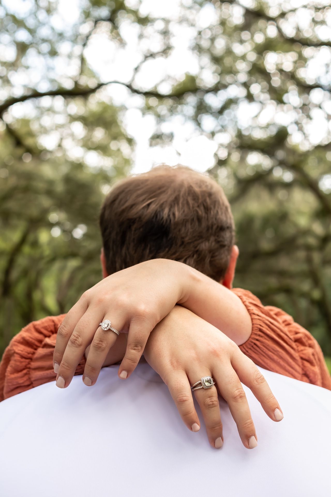 Three people pictured from behind resting their heads together with engagement rings visible on their hands.