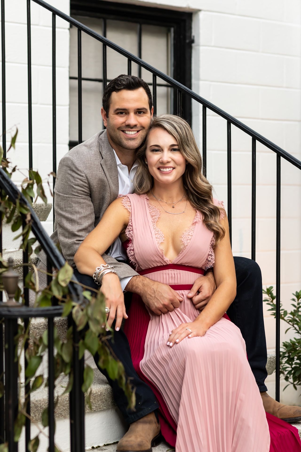 A couple in formal attire sits together on white steps with black railings in front of a building.