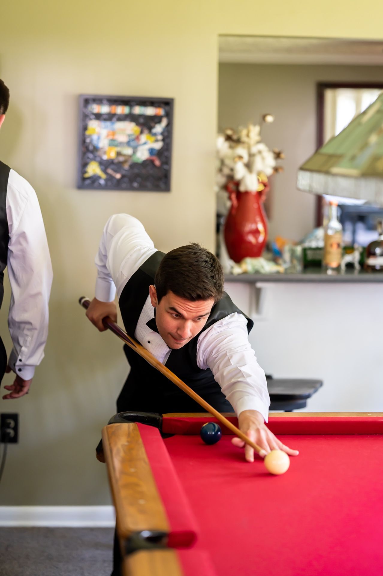 A player in a white shirt and black vest leans over a red pool table to line up a shot during a game of billiards.