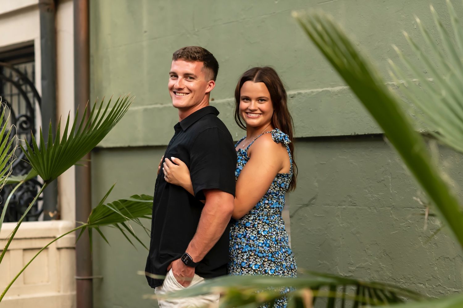 A couple laughs and embraces near tropical plants during an outdoor photo session.