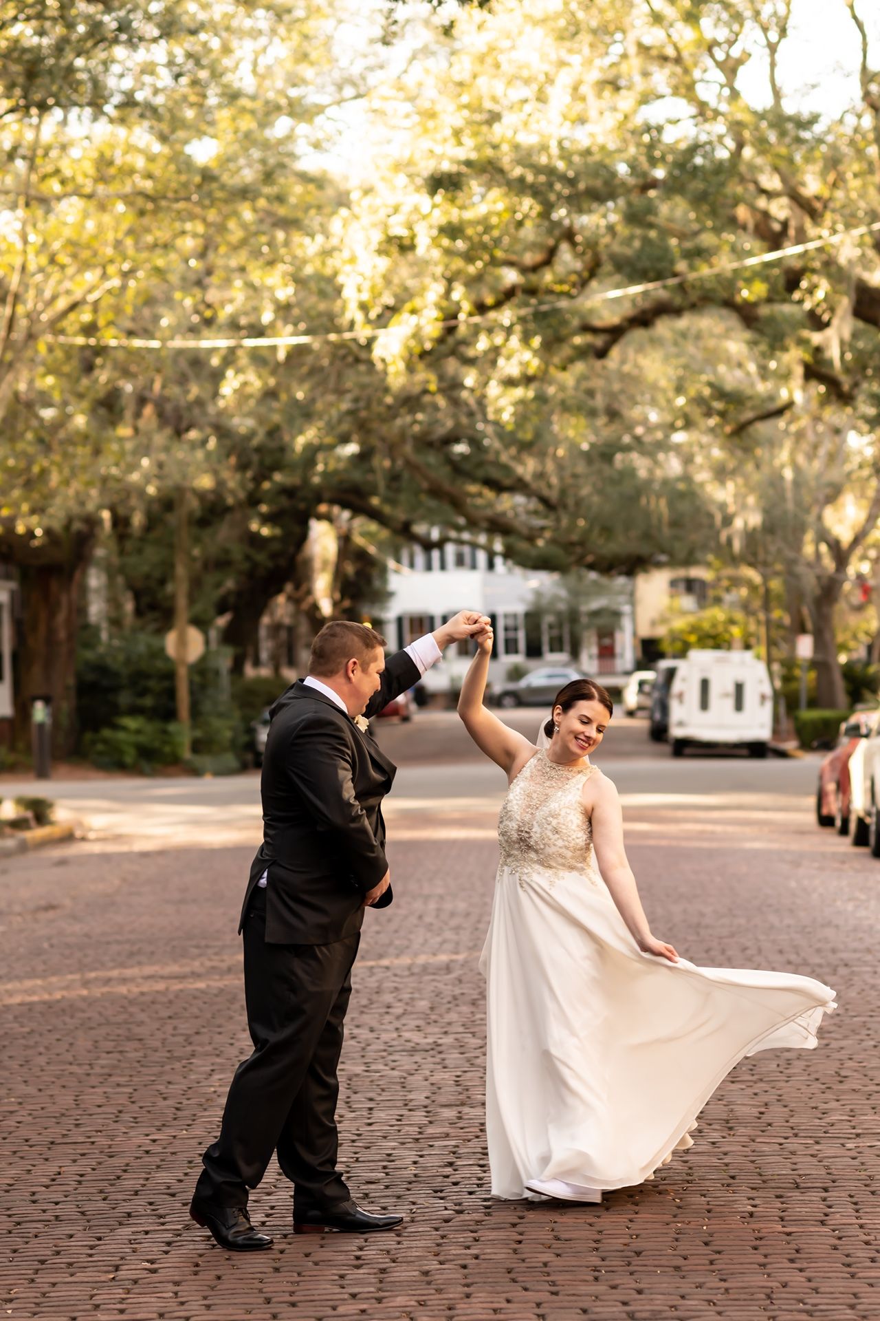 A couple enjoying a romantic dance on a brick-paved street at sunset with autumn trees in the background.