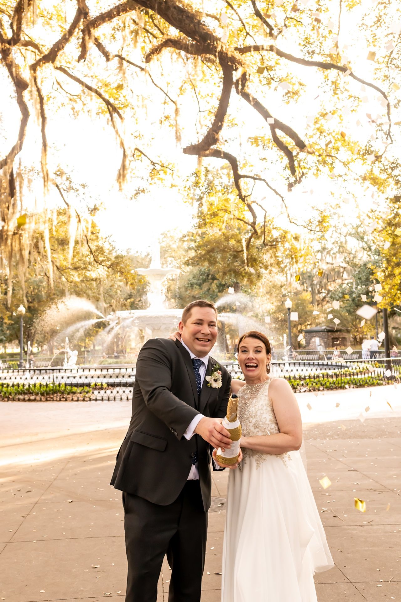 Newlywed couple laughs and plays with bubbles in a beautiful outdoor garden setting at sunset.