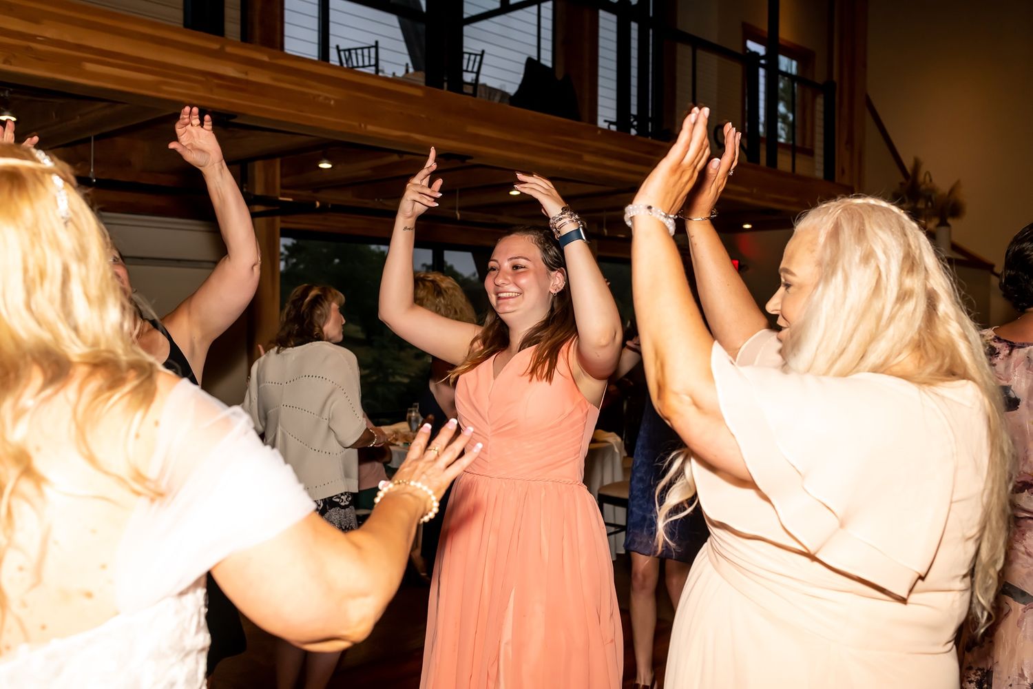 Three people in formal attire dancing with raised arms at a lively indoor celebration event.