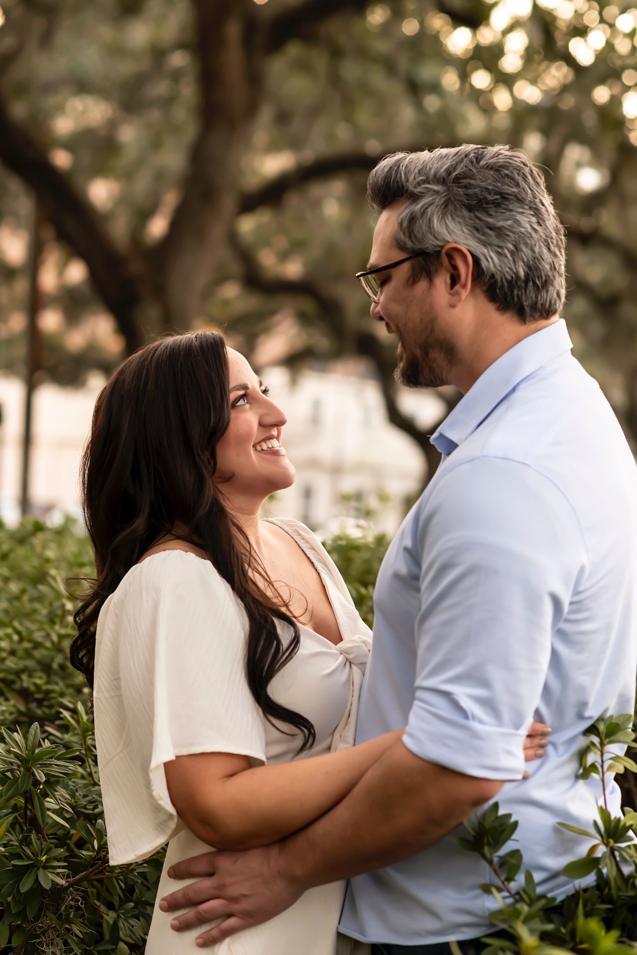 A romantic couple embraces while sharing a joyful moment together outdoors in a garden setting with bokeh lighting.