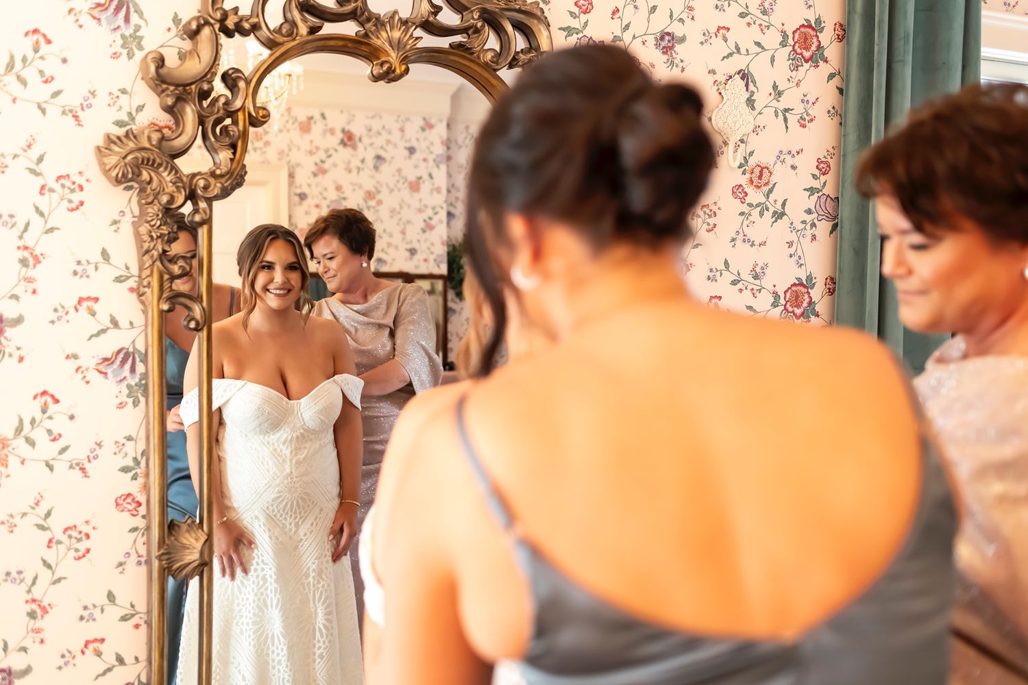 Bride and groom share a tender moment in front of a floral wallpapered wall at their wedding celebration.