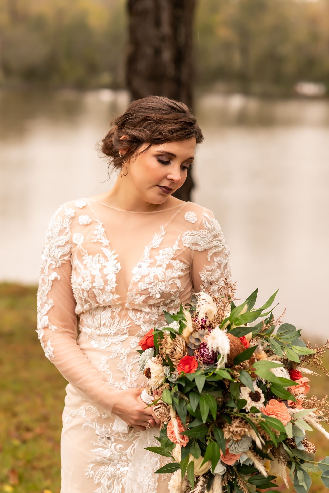 An elegant bridal photo shows a lace sleeve wedding dress and a vibrant bouquet of red and pink flowers with eucalyptus.