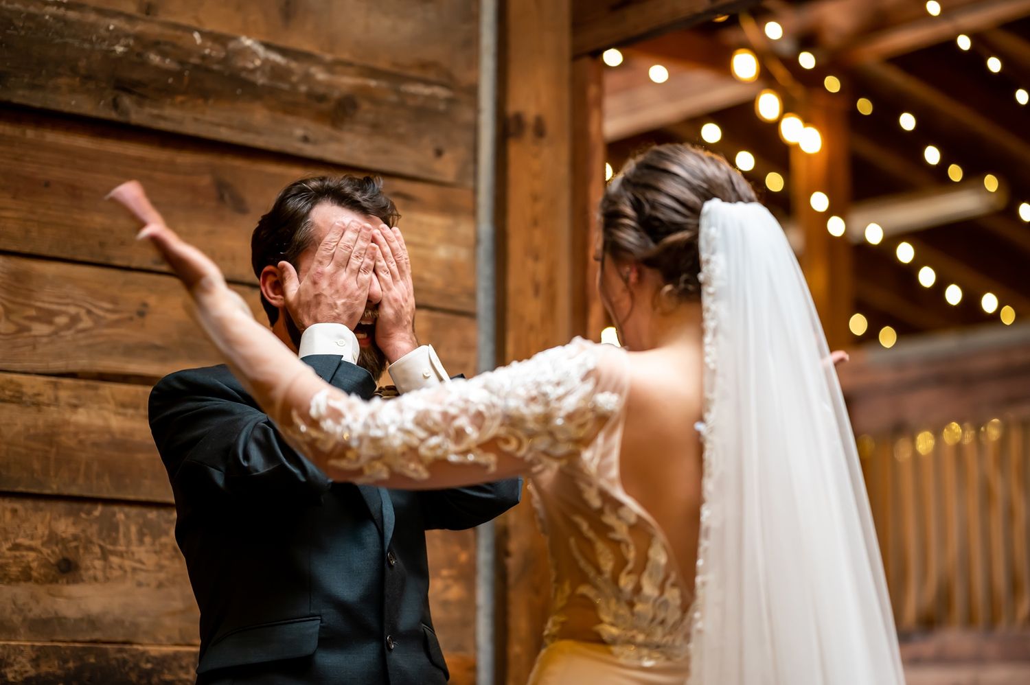 An emotional first look moment between newlyweds in a rustic barn venue decorated with twinkling string lights.