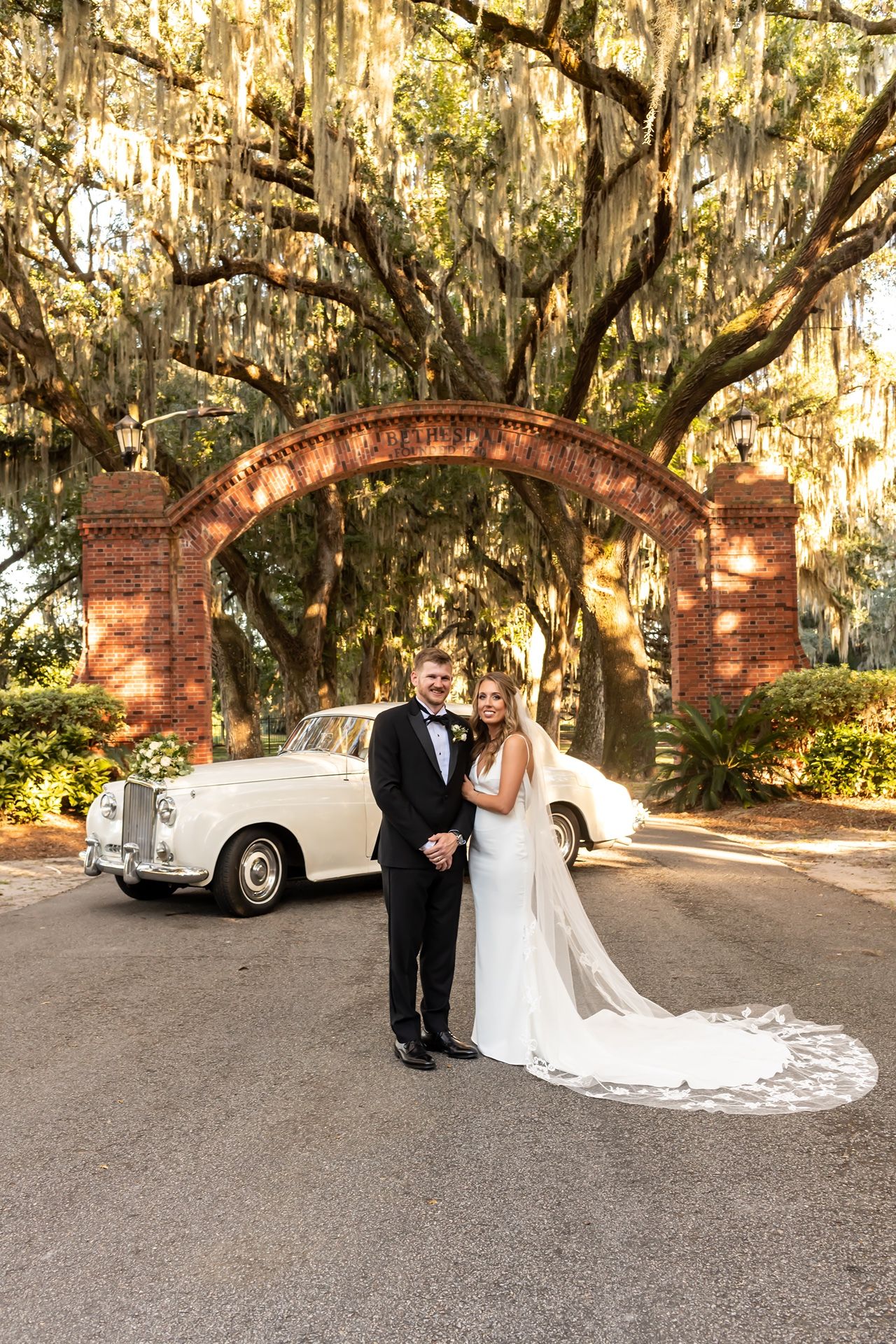 A romantic Southern wedding portrait series under moss-draped oak trees with a classic vintage car in the background.