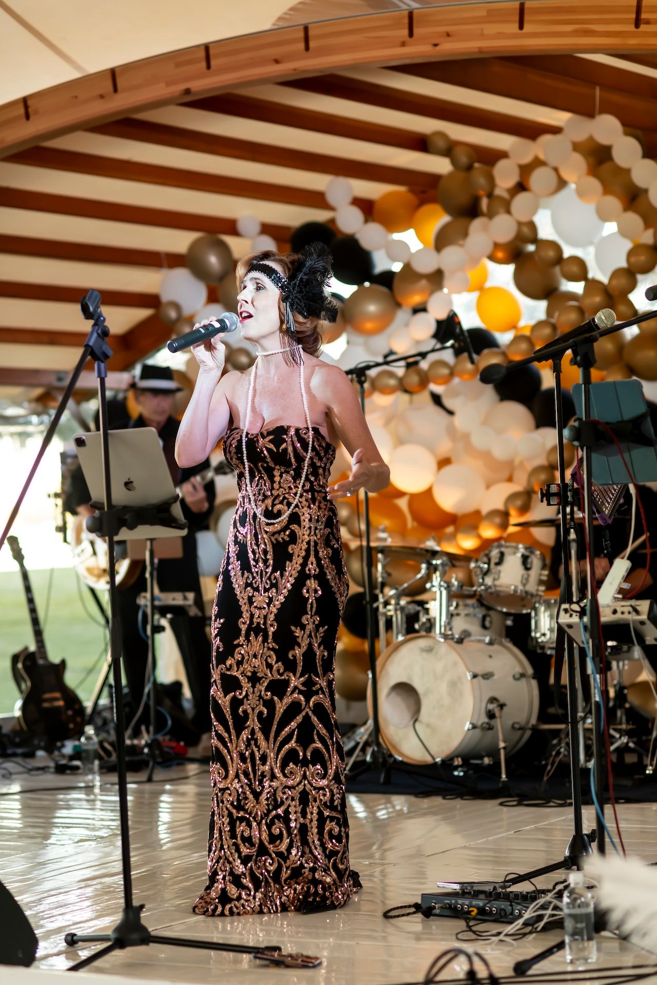 Singer performs in an elegant beaded gown on stage with balloon decorations and band equipment visible in background.