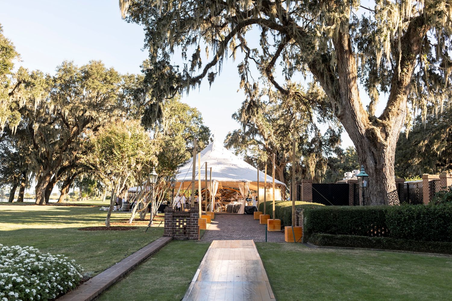 A scenic outdoor wedding venue with Spanish moss-draped oak trees and a paved walkway leading to a covered pavilion.