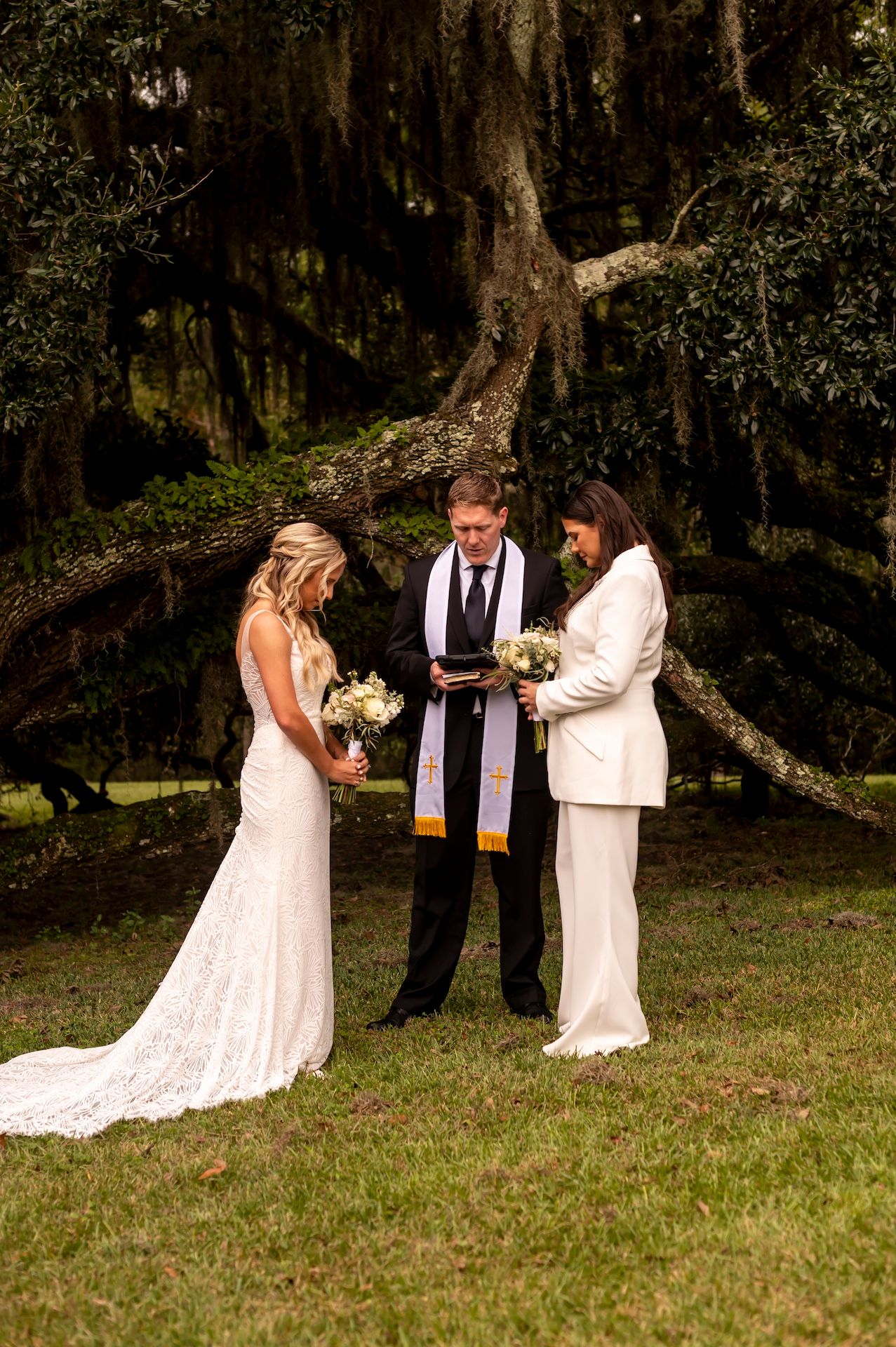 An outdoor wedding ceremony unfolds under moss-draped trees in a natural woodland setting.