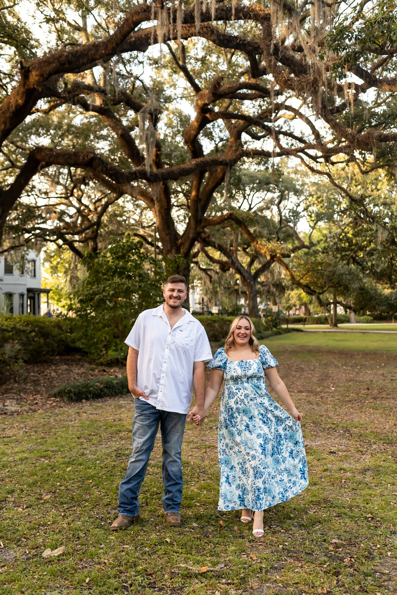 A couple stands together under massive oak trees draped with Spanish moss.