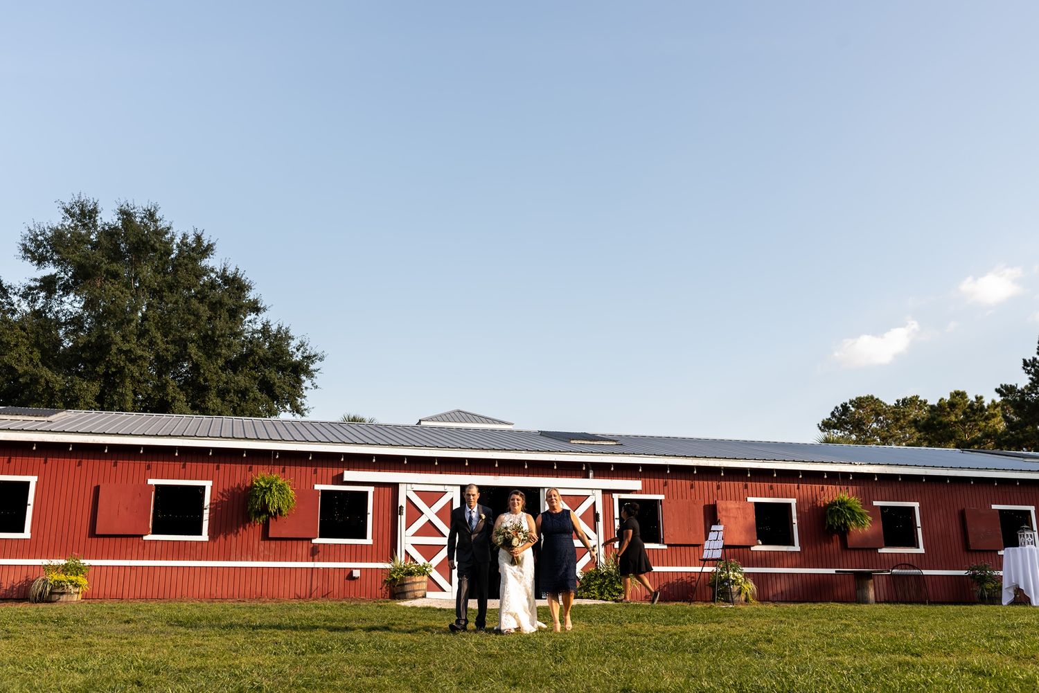 A red barn with white trim serves as a backdrop on a sunny day with green grass and blue skies.