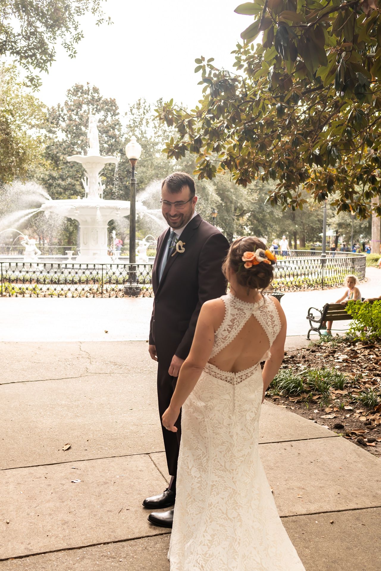 A romantic wedding moment in front of a fountain as newlyweds stand together in a park-like setting on a sunny day.