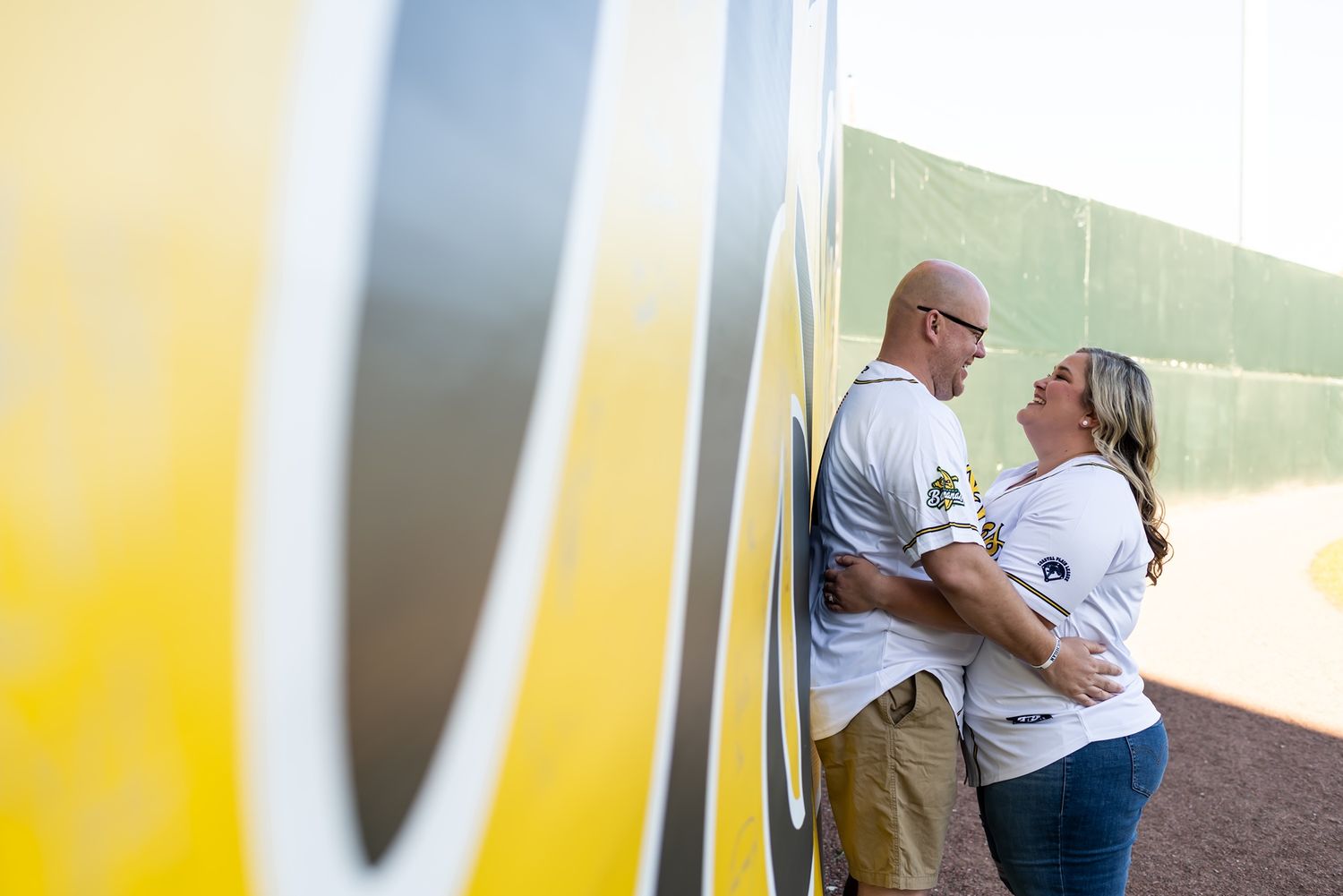 A couple in white shirts shares an intimate moment leaning against a colorful wall outdoors.