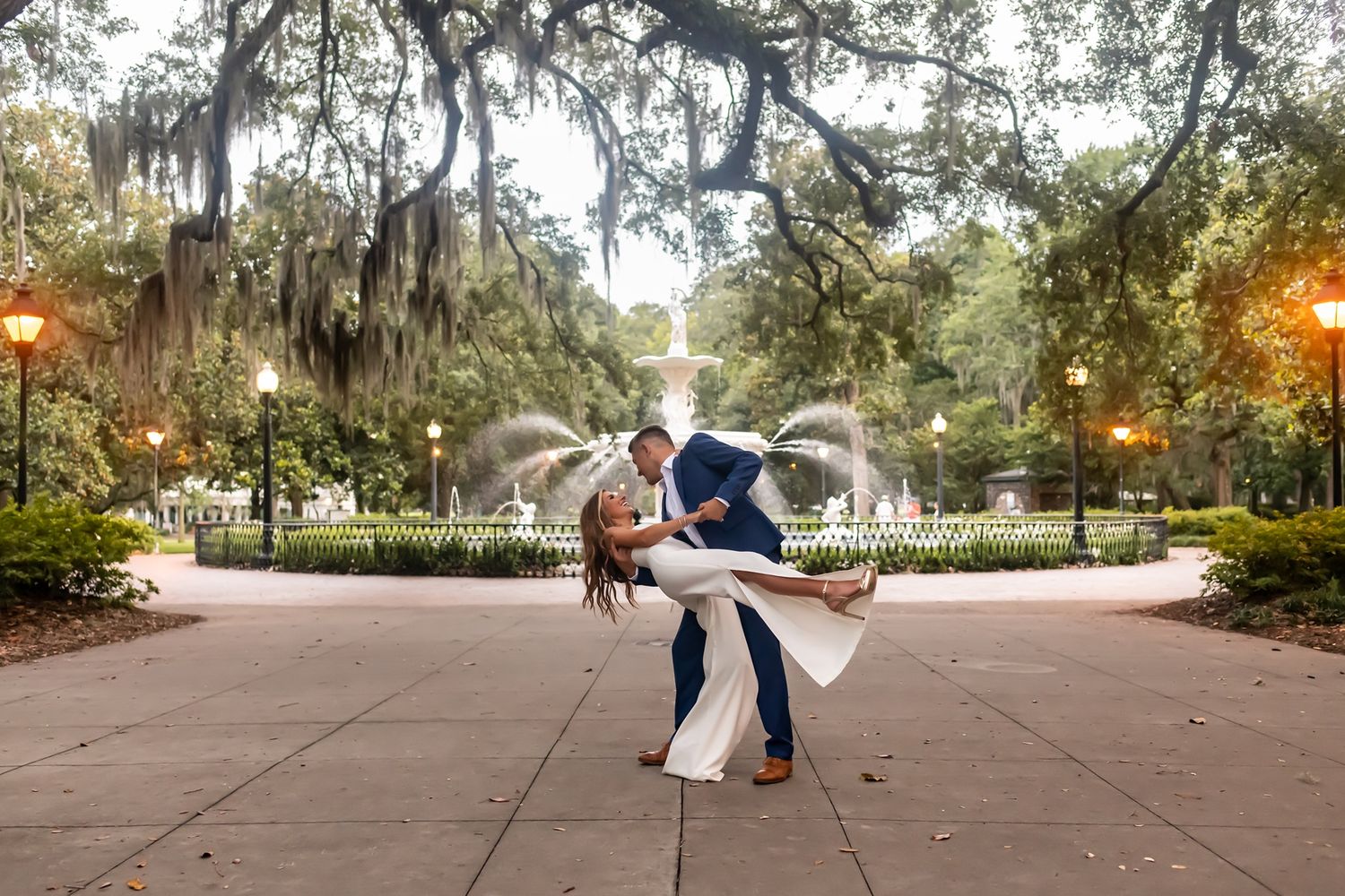 A romantic couple shares an intimate dance dip pose in a beautiful Spanish moss-draped park at sunset.