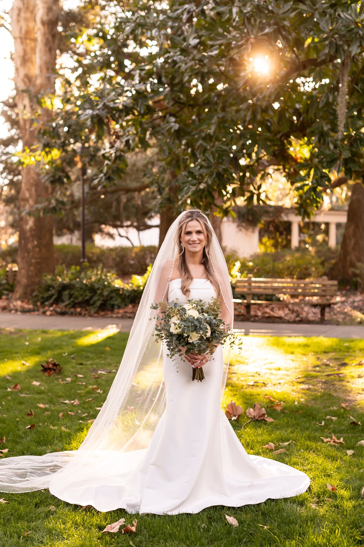 Sunlit outdoor bridal portraits on green lawn with flowing white dress and floral bouquet.