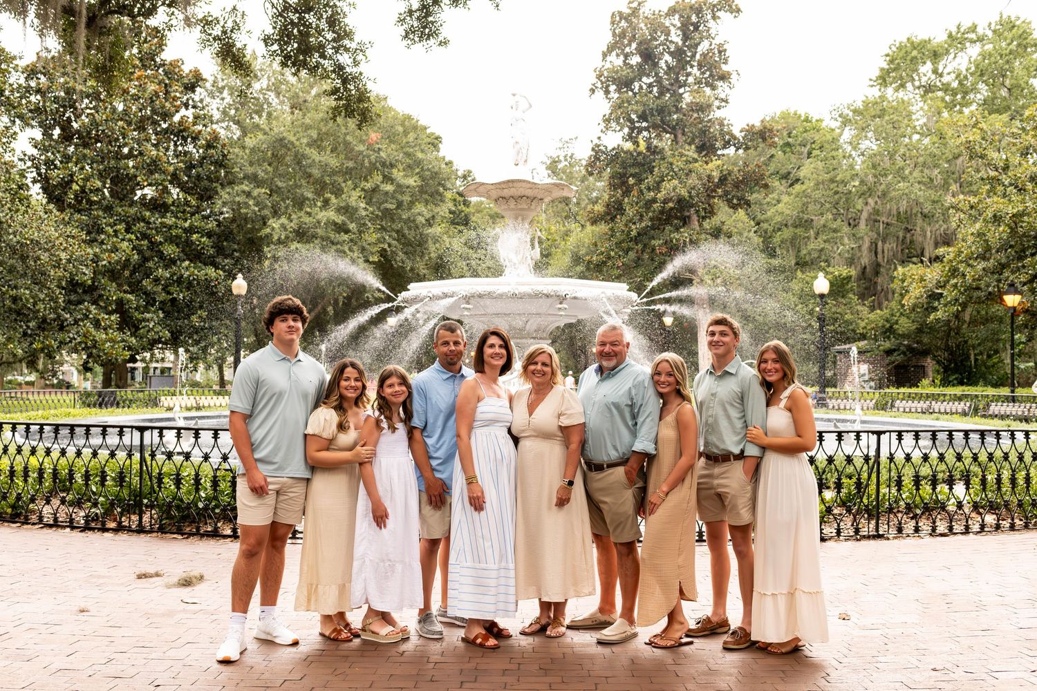 Wedding party in pastel colors poses for a group panoramic photo on a sunny day in a garden setting.