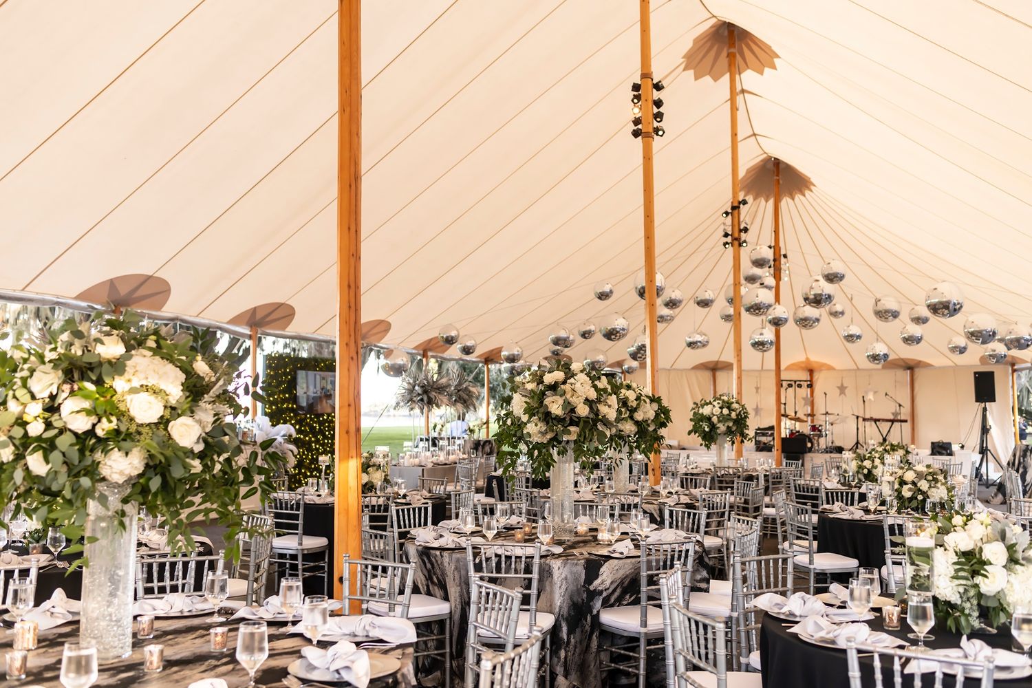 Elegant wedding tent reception with white floral centerpieces, silver chiavari chairs and hanging bamboo lanterns overhead.