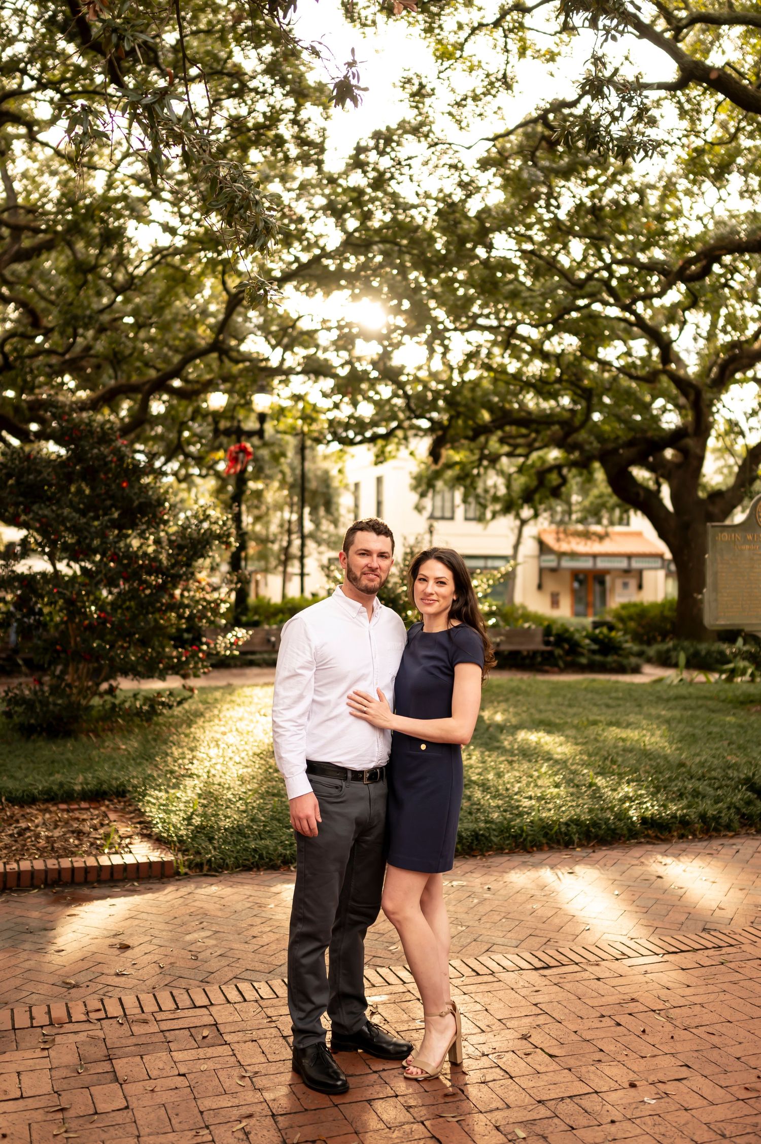 A romantic dance sequence on a red brick pathway under a canopy of trees at sunset.