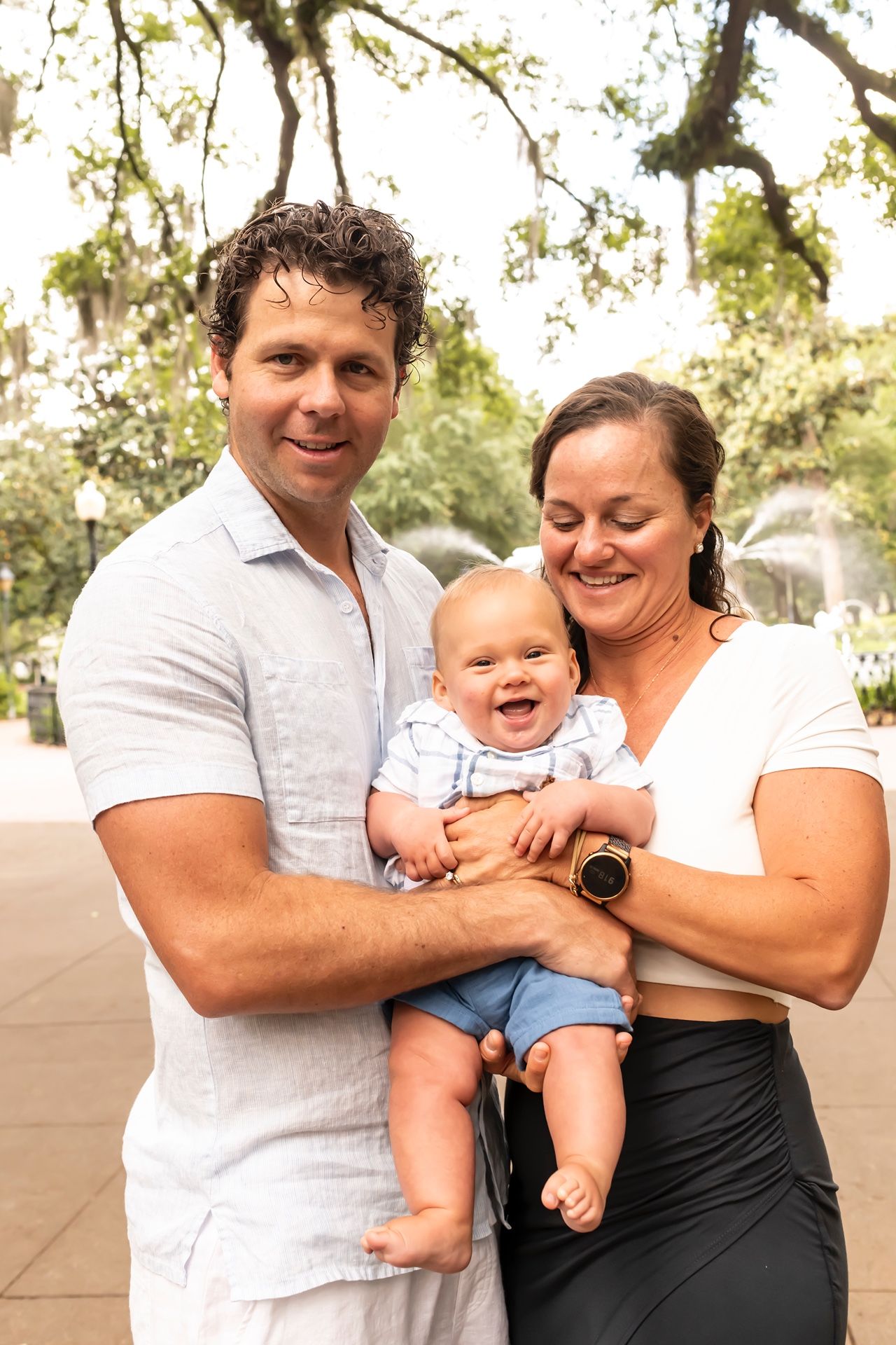 A happy family shares a joyful moment together outdoors on a sunny day with trees in the background.