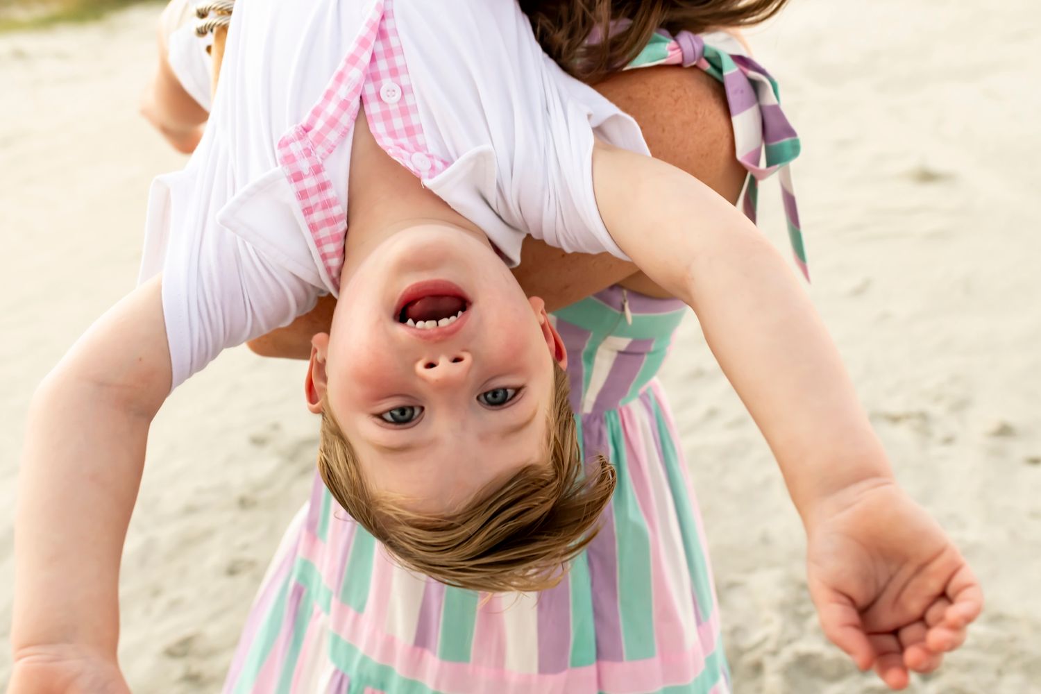 Three siblings in matching striped dresses play and laugh together at the beach.