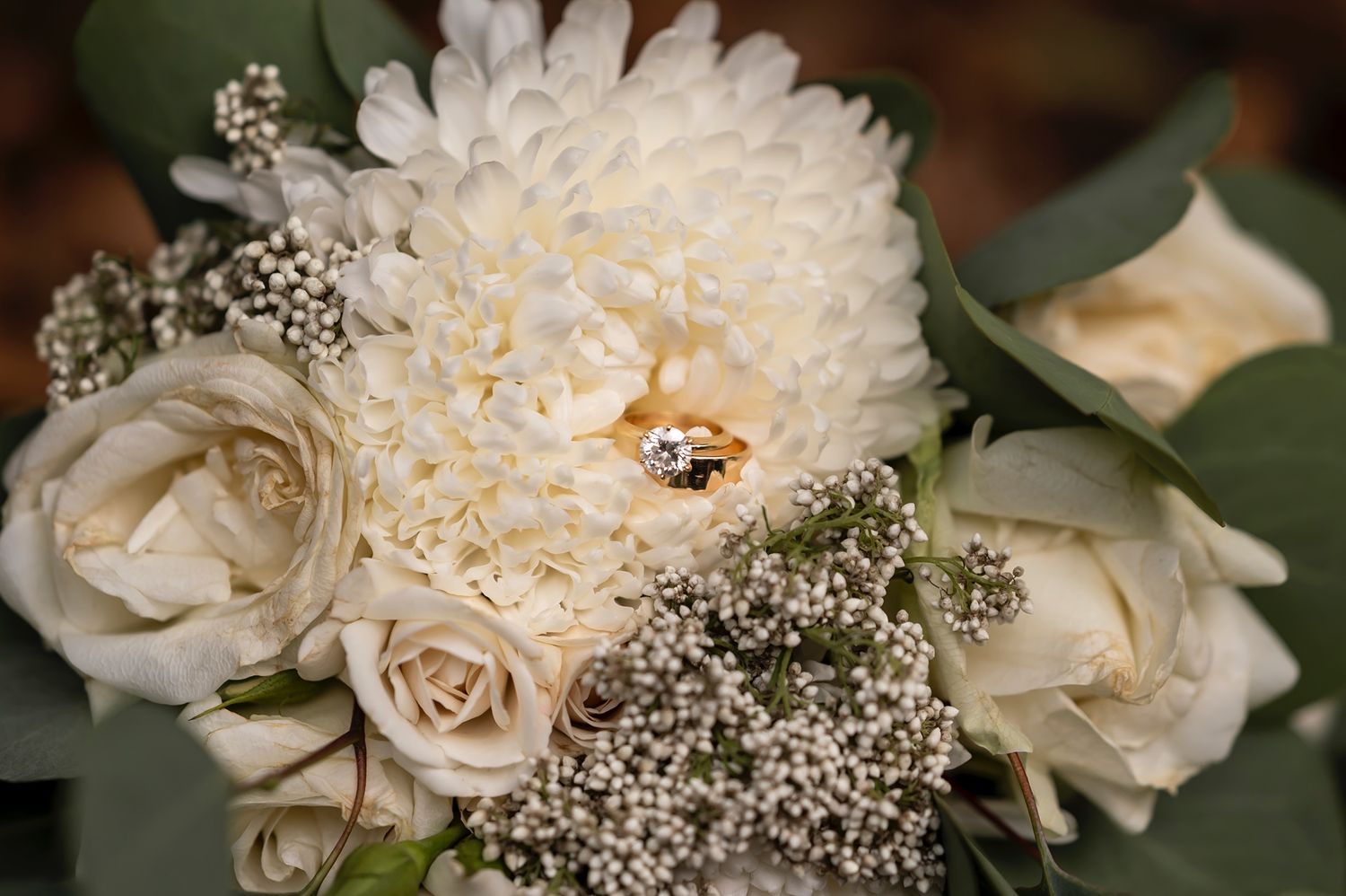 Close-up of an elegant bridal bouquet featuring cream roses, white chrysanthemums and delicate baby's breath flowers.