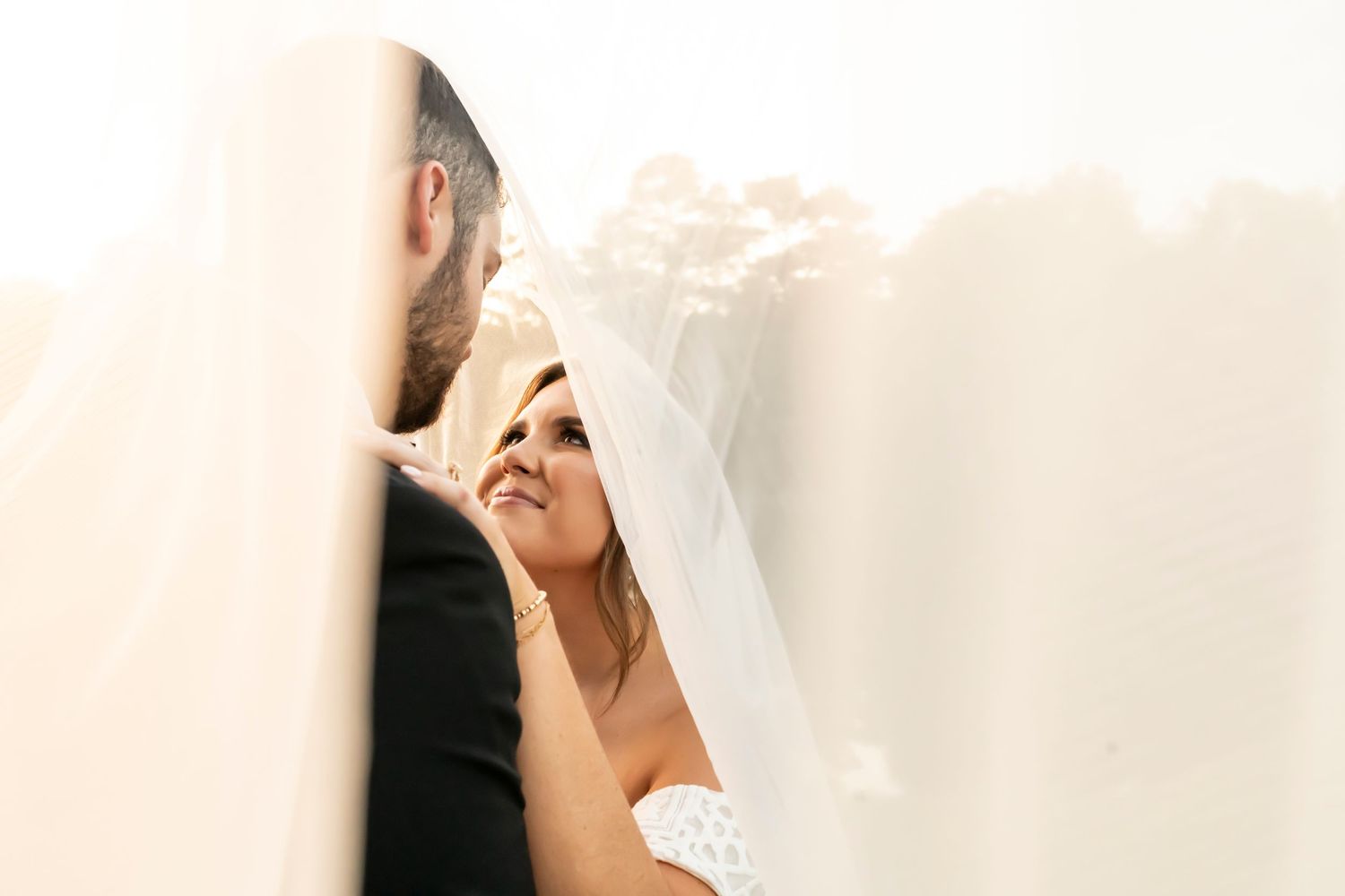 A tender moment between newlyweds as they share an intimate exchange under the bride's flowing white veil.
