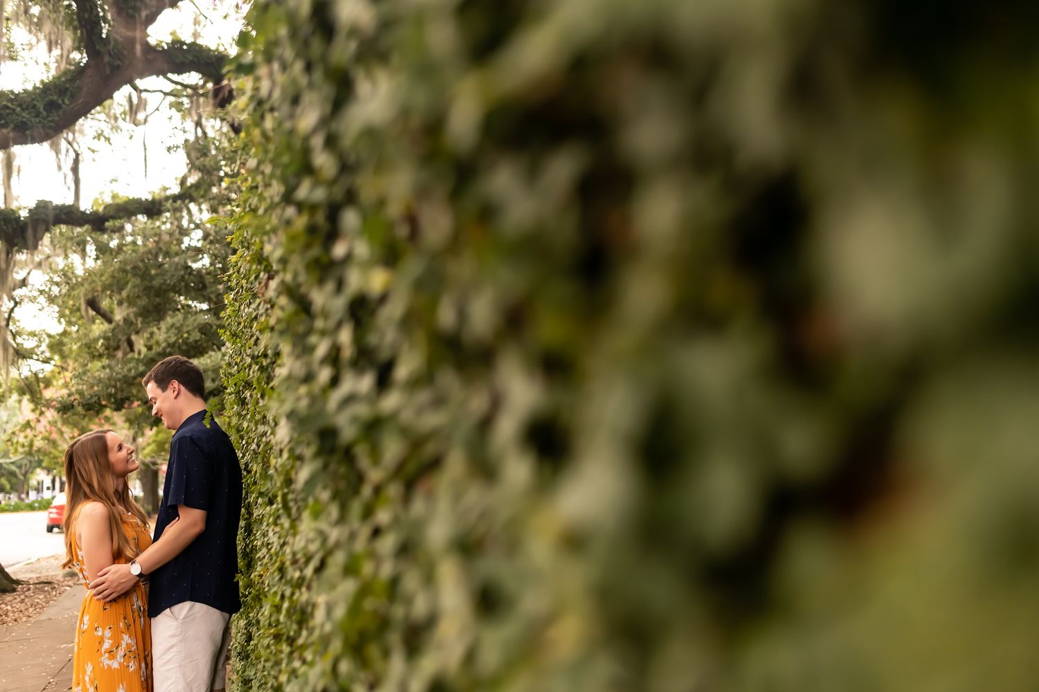 A couple shares an intimate moment outdoors surrounded by lush greenery and natural sunlight.