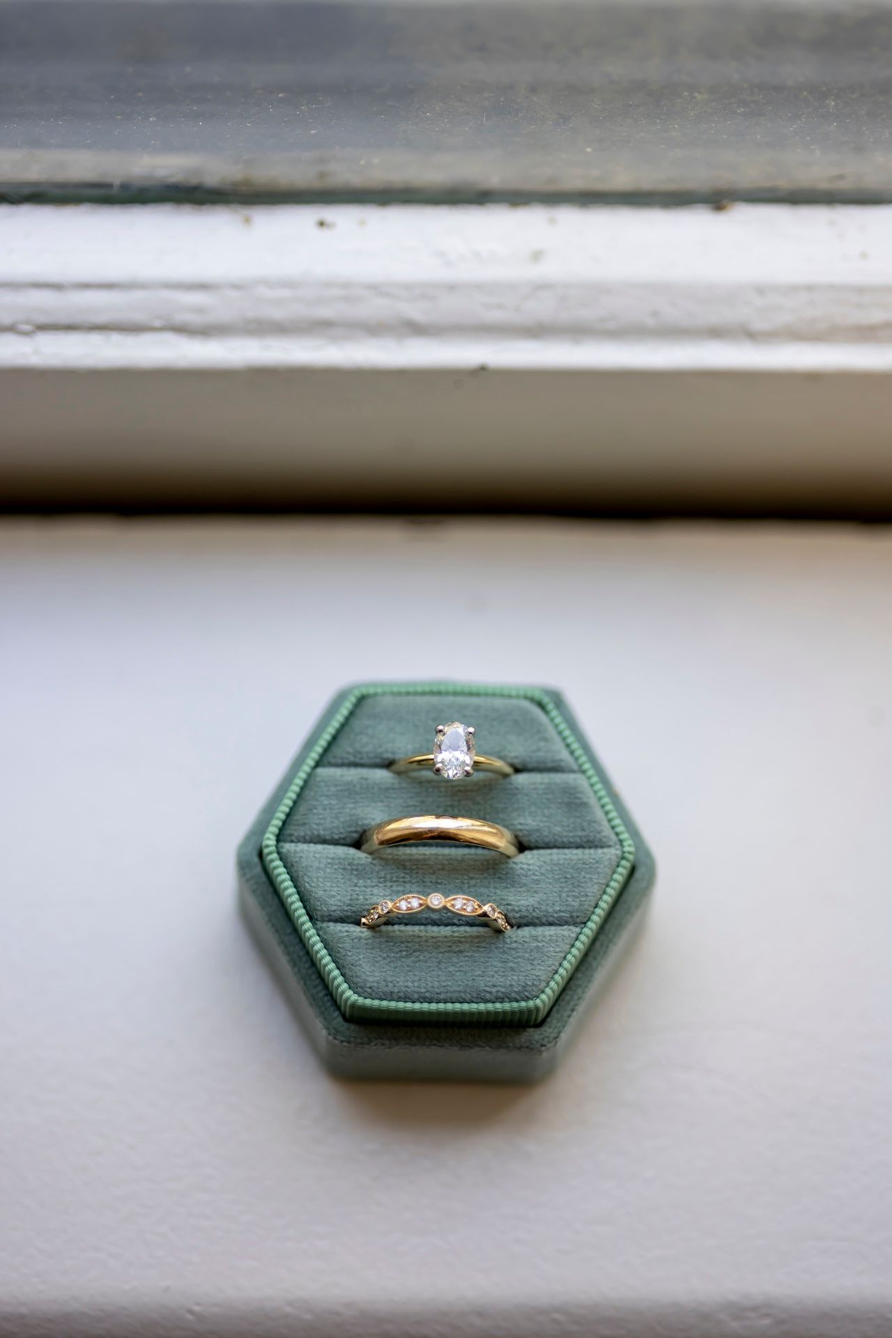 Three wedding rings displayed on a green hexagonal velvet ring holder box against a white surface.