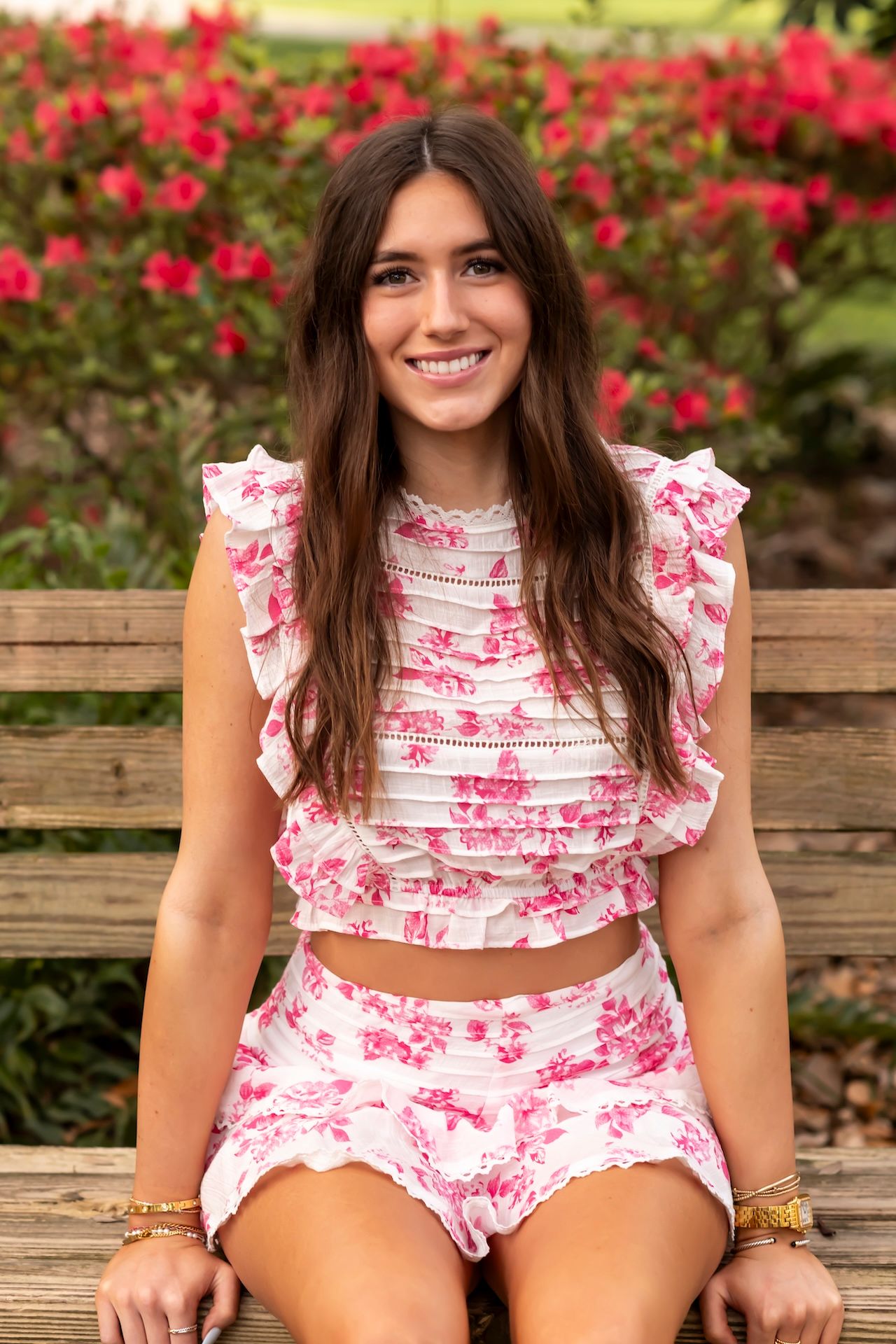 A pink floral two-piece summer outfit showcased against a backdrop of bright red flowering bushes.