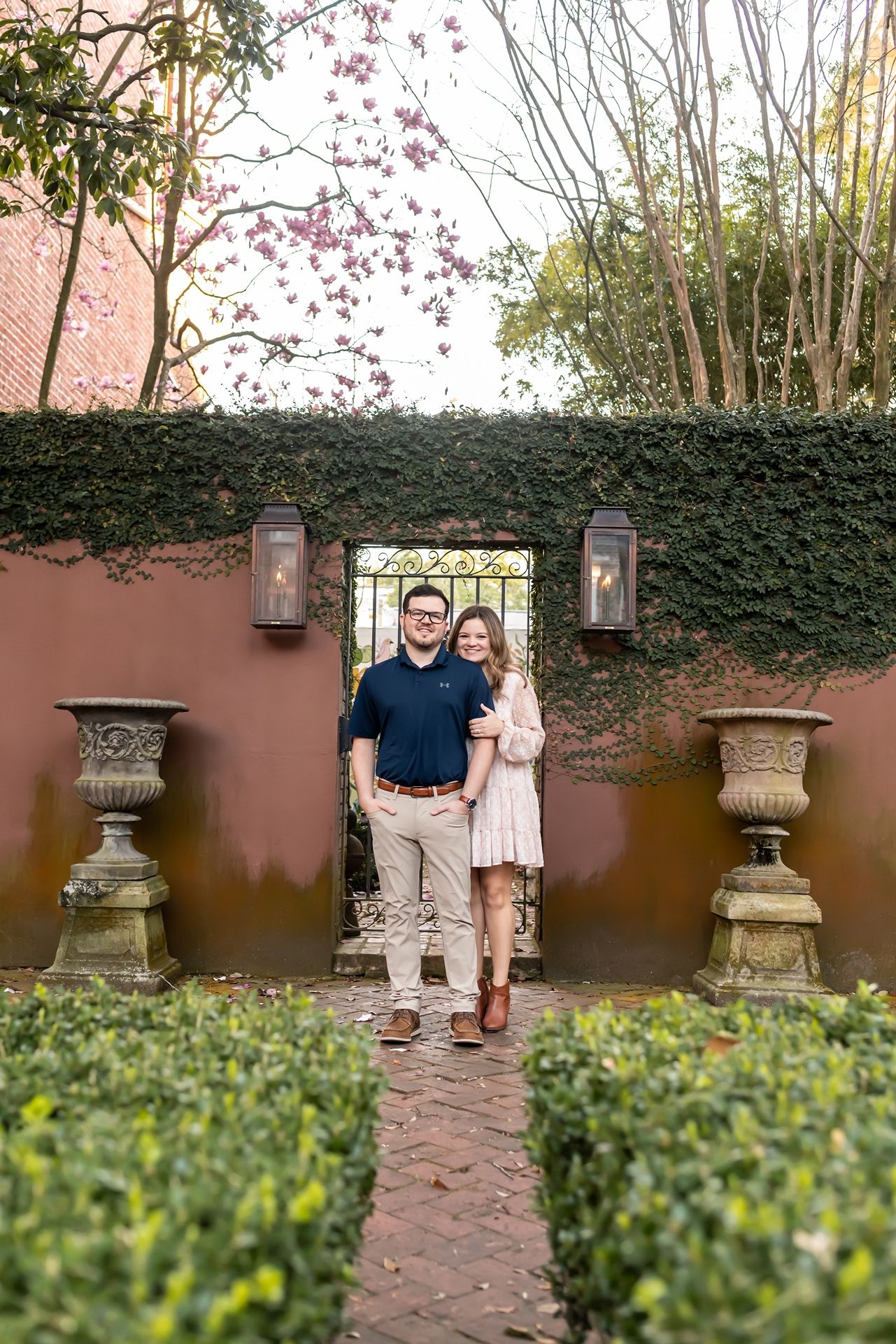 A romantic garden scene with brick pathway, ivy-covered walls, lanterns and stone urns in a courtyard setting.