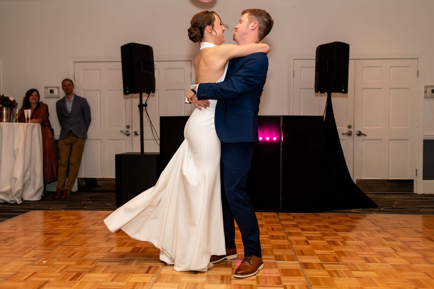 Couple shares an intimate first dance on parquet floor with speakers and lighting setup at wedding reception.