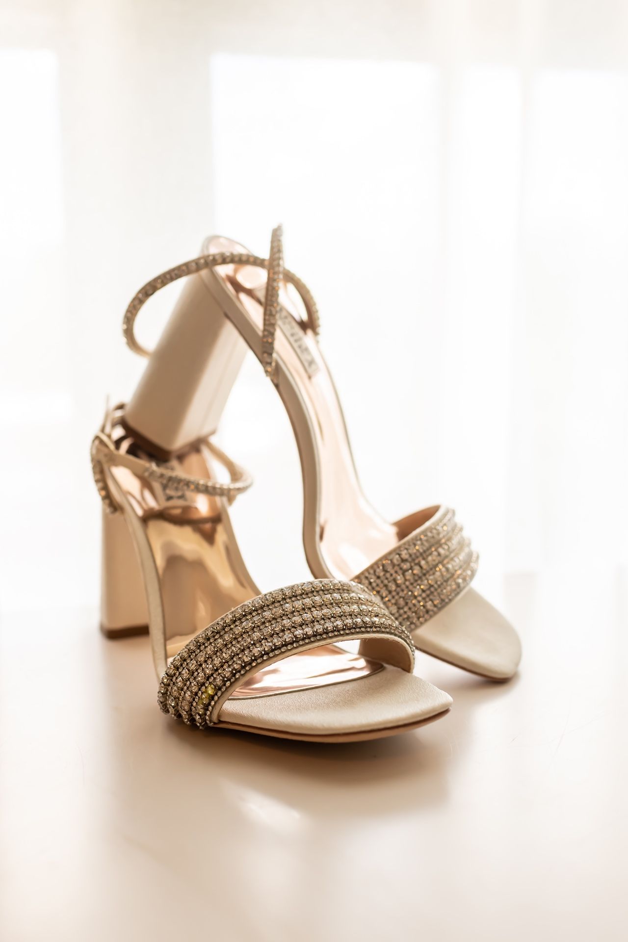Elegant bridal heels in metallic gold with crystal embellishments and ankle straps on white surface.