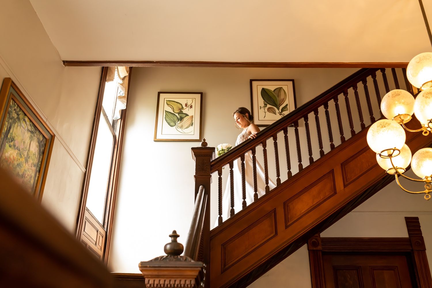 A wooden staircase with ornate railings ascends under warm lighting in a classic Victorian-style interior setting.