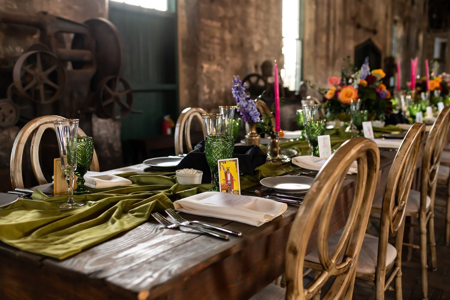 Rustic wooden dining tables and chairs are set up in a dimly lit venue with elegant table settings and decor.