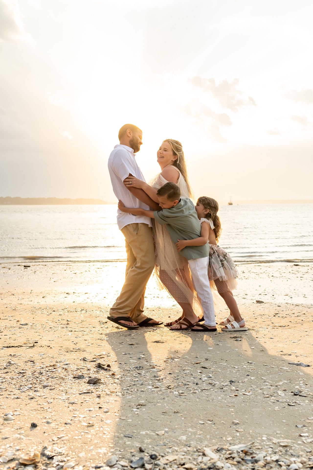 Family plays together on sandy beach at sunset with gentle ocean waves in the background.