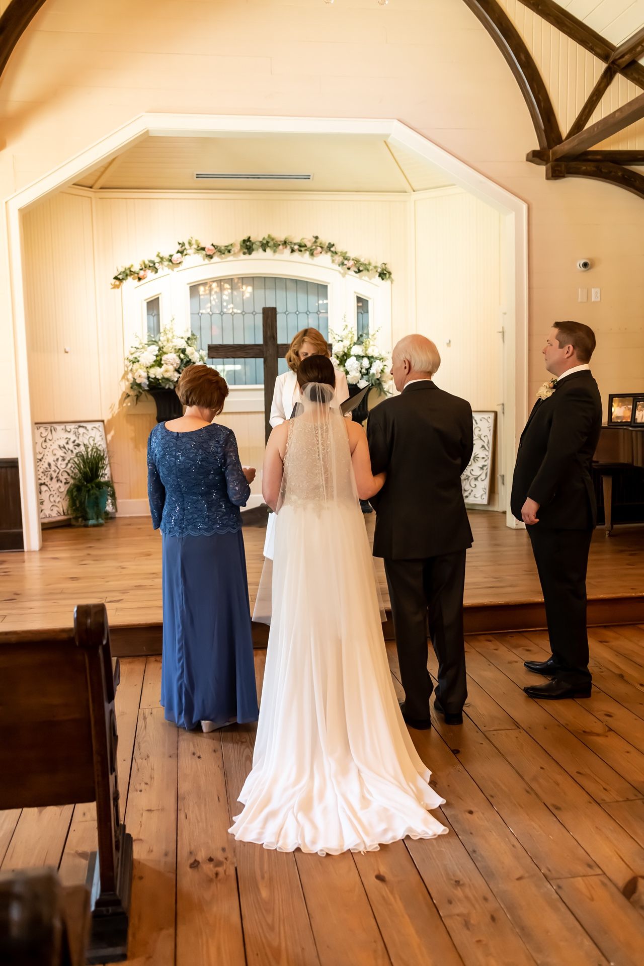 Wedding party preparing for ceremony in an elegant chapel with hardwood floors and arched ceiling.