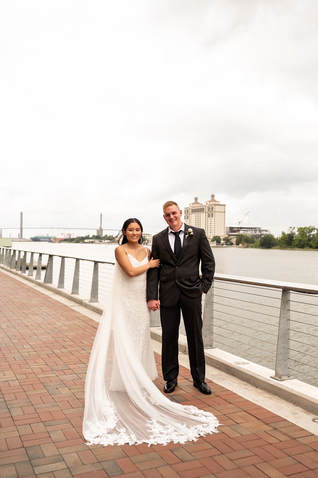 A couple poses together for wedding photos on a waterfront brick terrace with scenic views in the background.