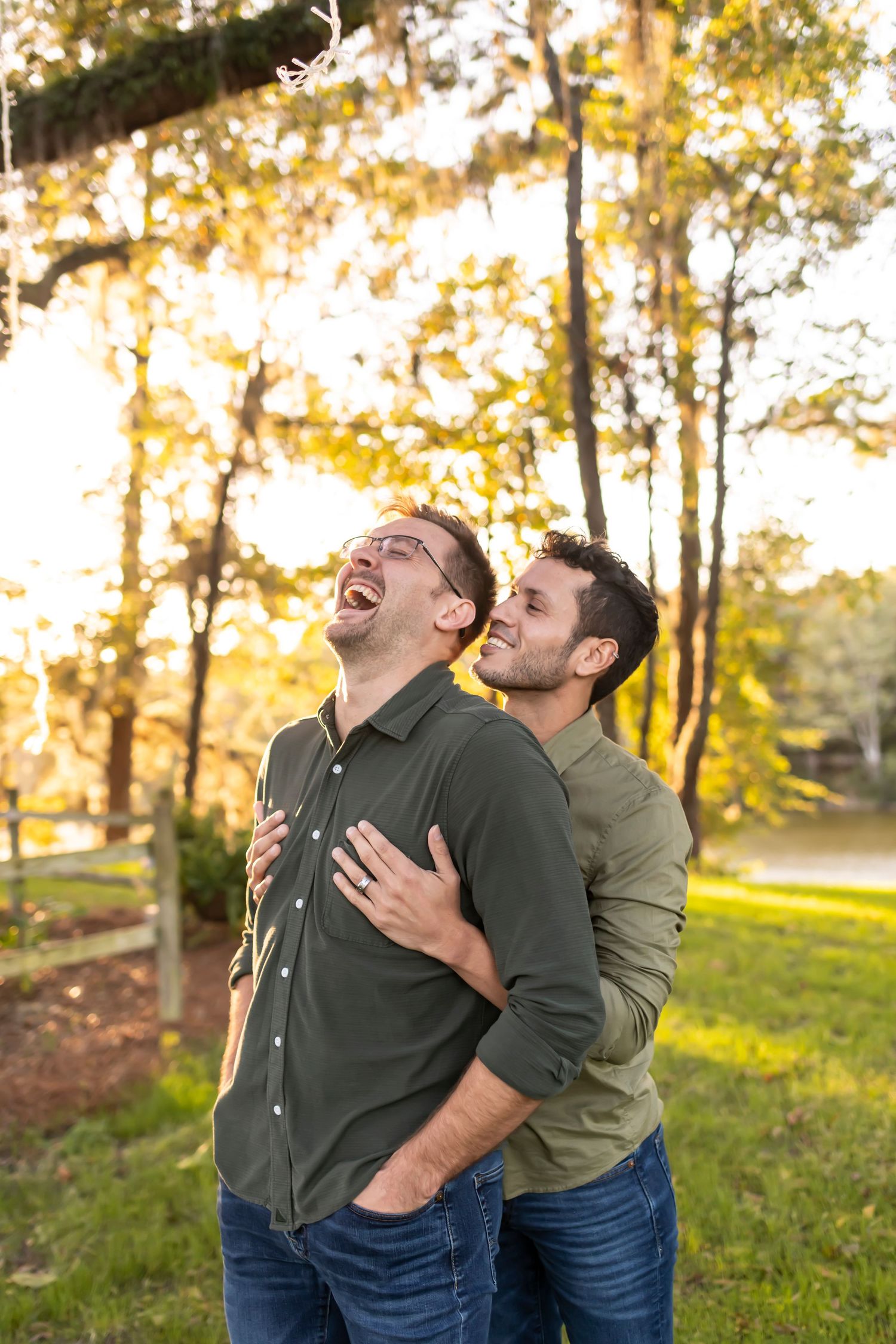 Two same-sex people share a joyful moment together outdoors with golden sunlight filtering through autumn trees.
