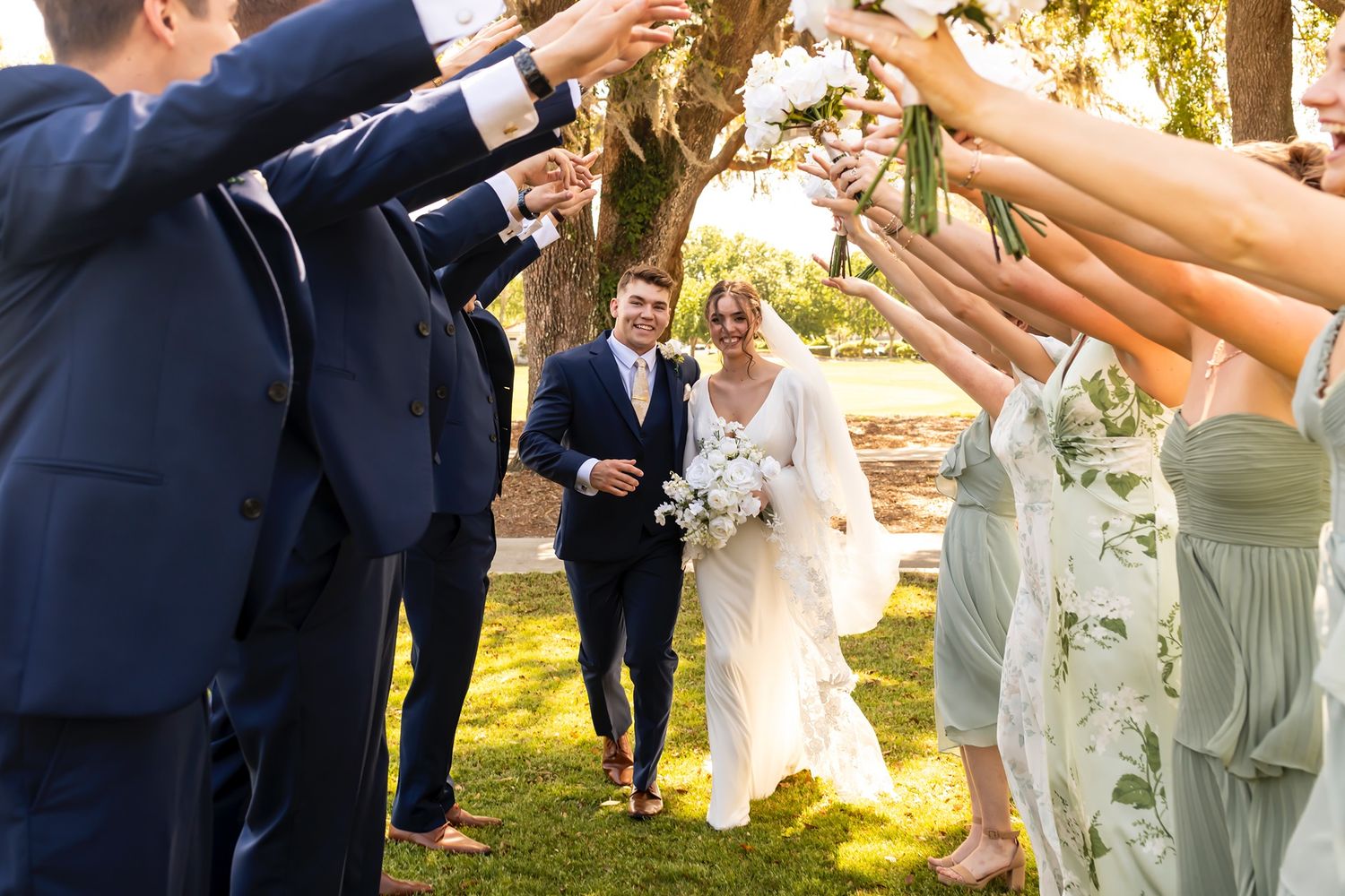 Wedding guests form a human tunnel outdoors while the newlyweds walk underneath during sunset celebrations.