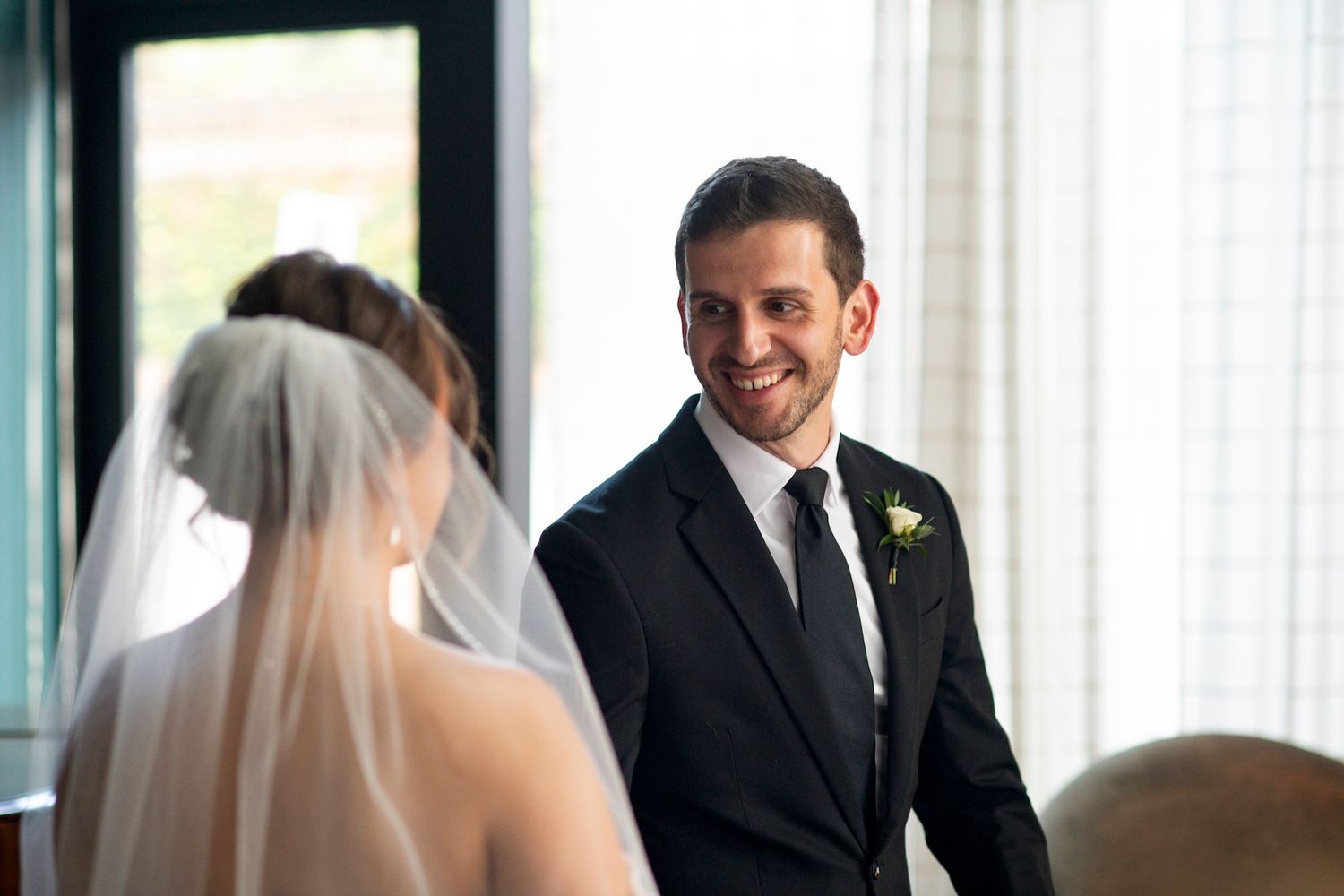 A bride and groom share a joyful moment during their wedding ceremony in a bright, window-lit venue.